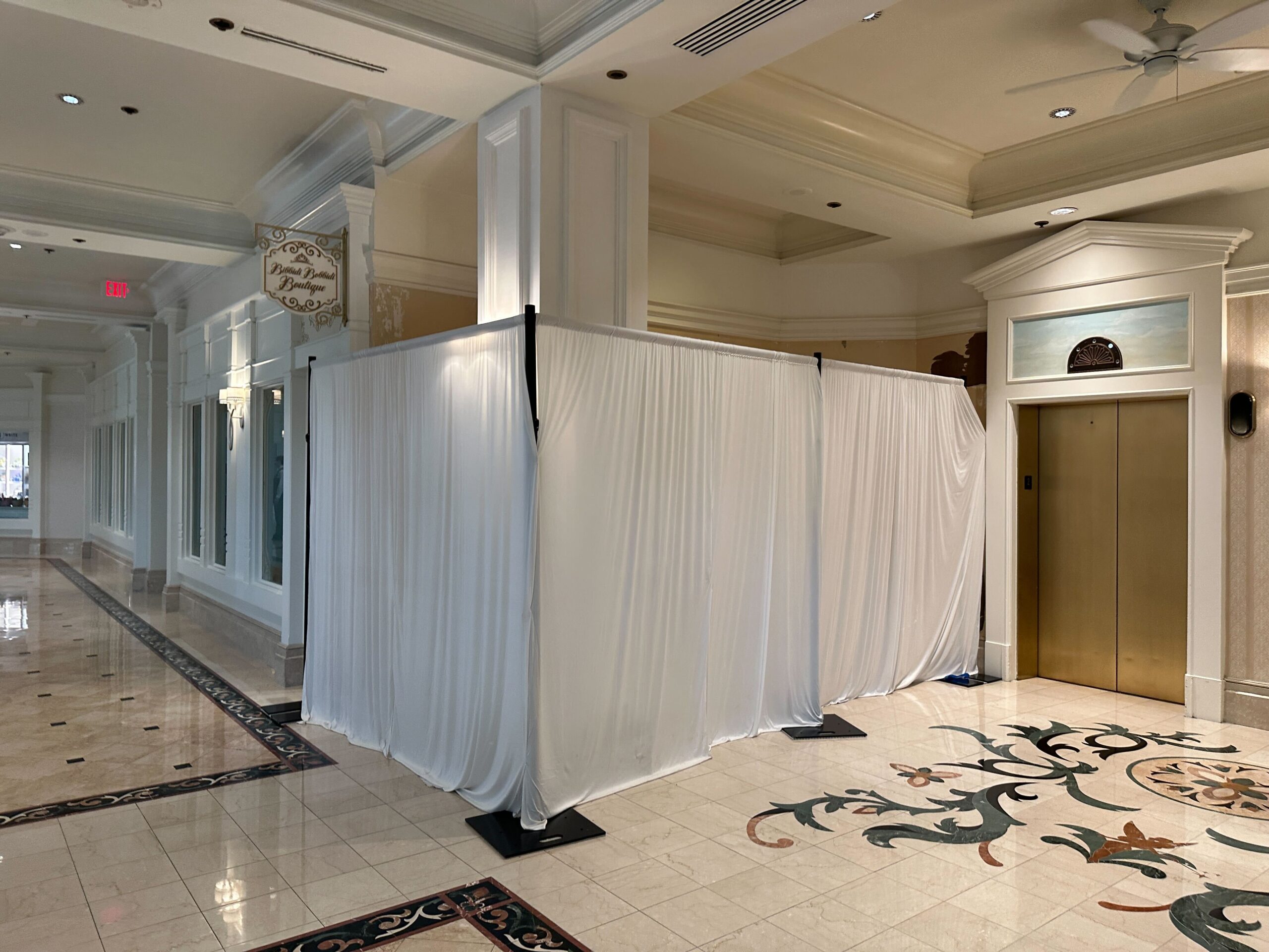 White drapes enclose a section of a hotel hallway near an elevator, likely blocking off construction or renovations.