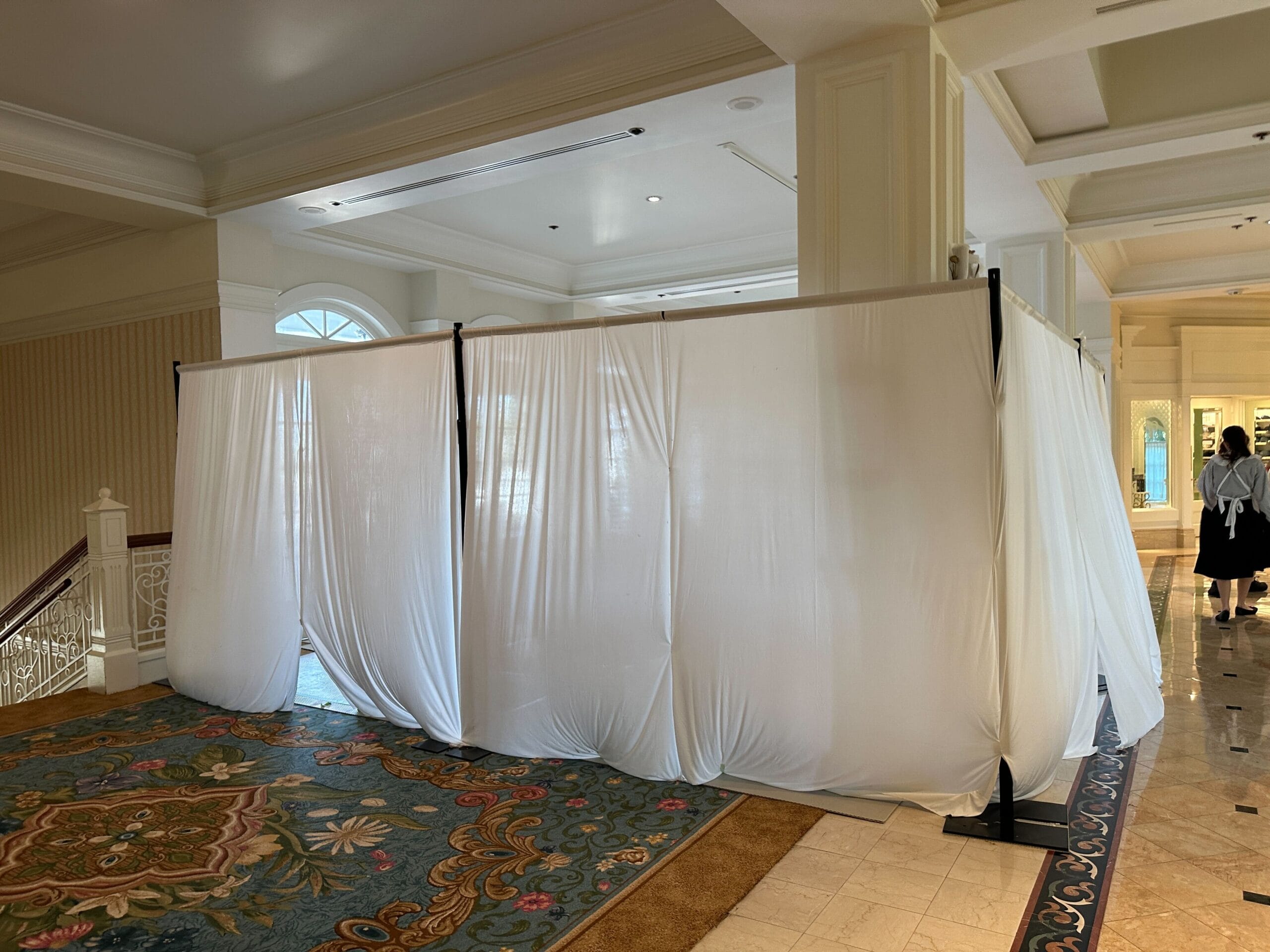 A white fabric curtain enclosure stands in a hotel lobby, partially blocking a hallway and staircase.