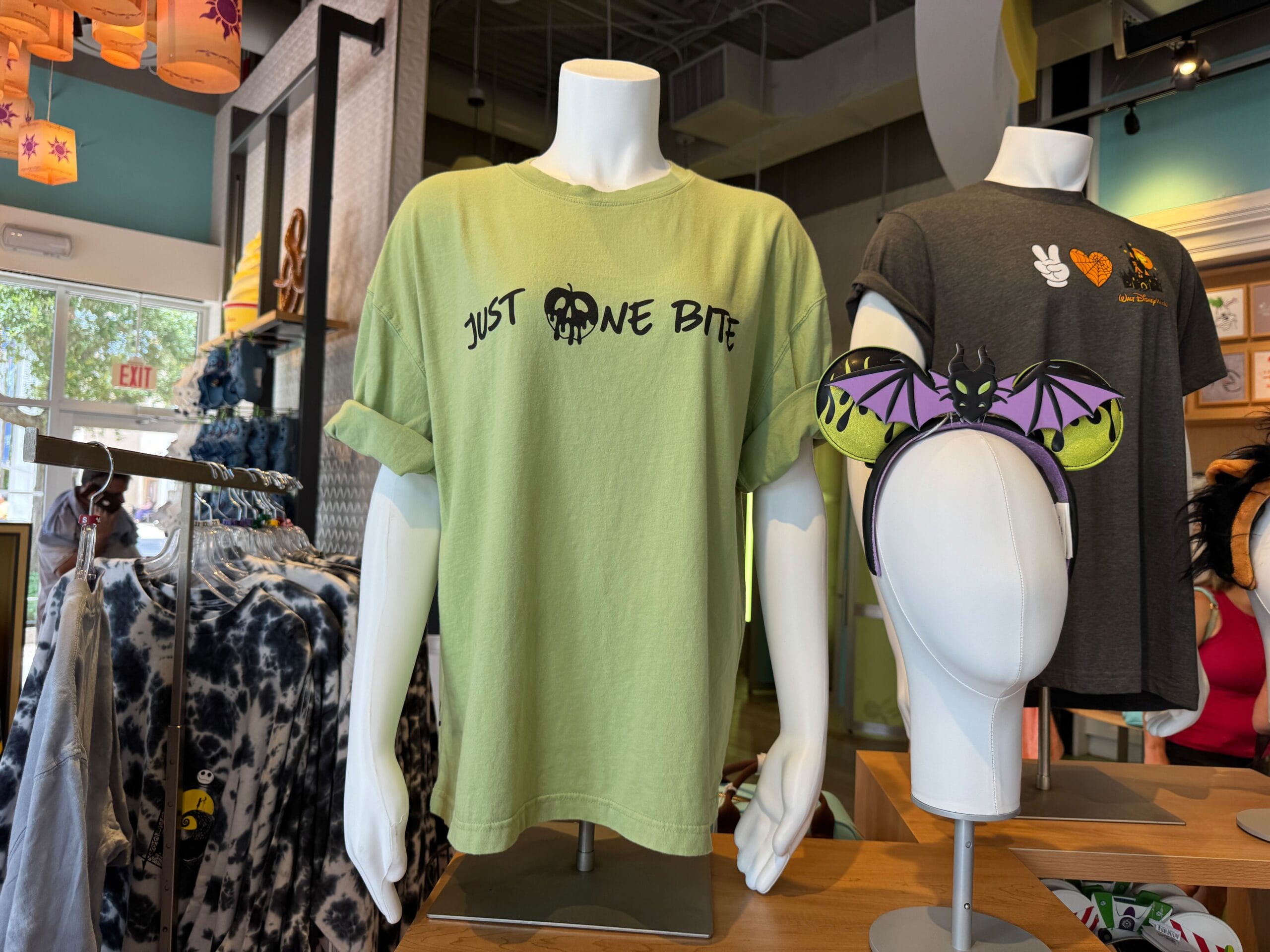 Light green t-shirt on mannequin with "Just One Bite" text and skull apple graphic, displayed in a store.