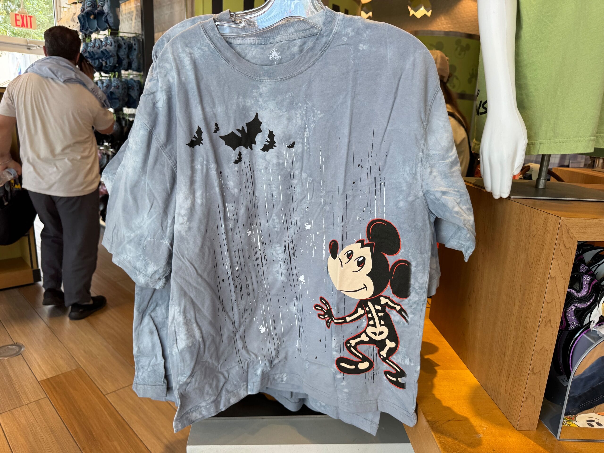 Gray T-shirt featuring a skeleton Mickey Mouse and flying bats, displayed on a rack in a retail store.