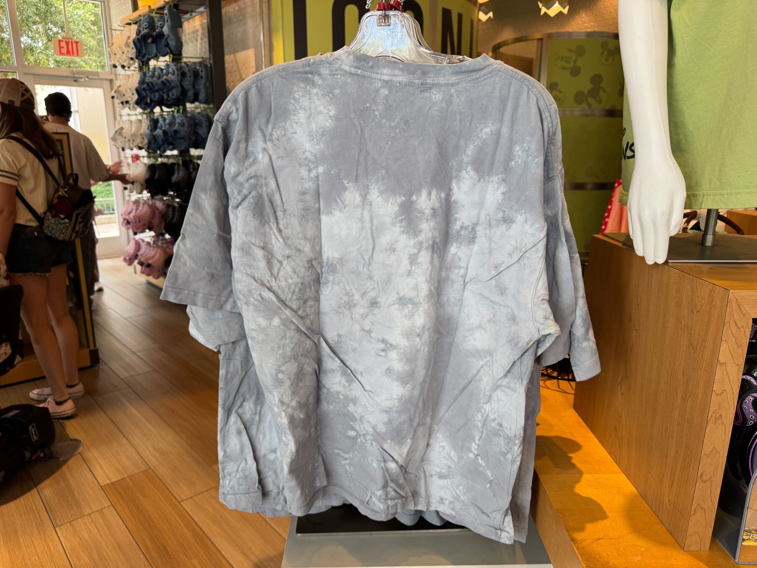 A gray tie-dye t-shirt displayed on a mannequin in a retail store with wooden floors and shelves.