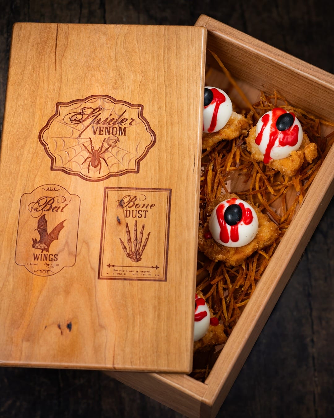 Jock Lindsey's Hangar Bar Halloween Wooden box with Halloween labels, partially open to reveal eyeball-shaped treats on a bed of shredded material.