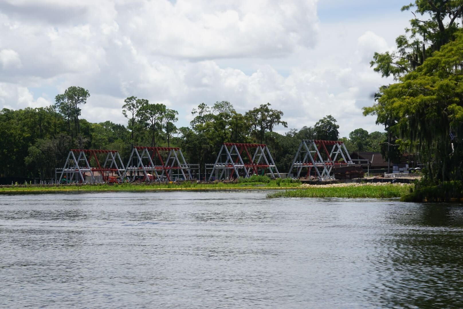 Four large metal swing bridge structures stand by the water, surrounded by trees under a partly cloudy sky.