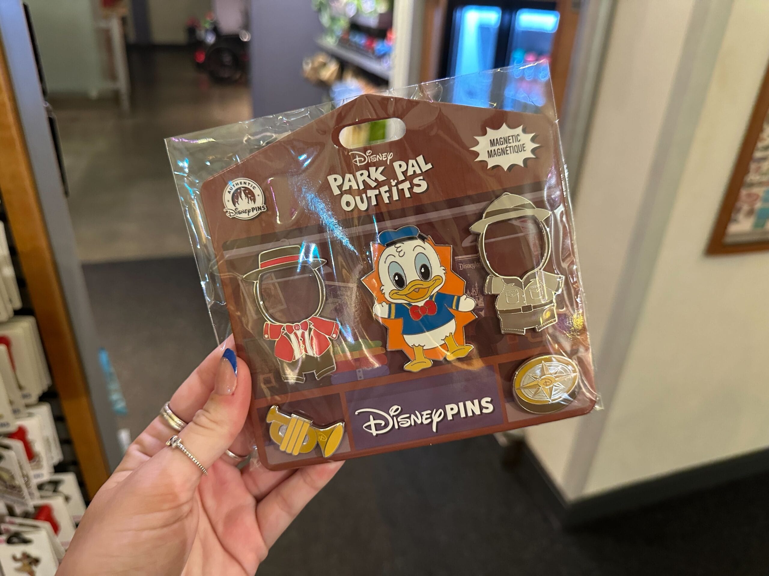 A hand holds a Disney Park Pal Outfits pin set with Donald Duck, two outfit pins, and collectible park pal outfits.