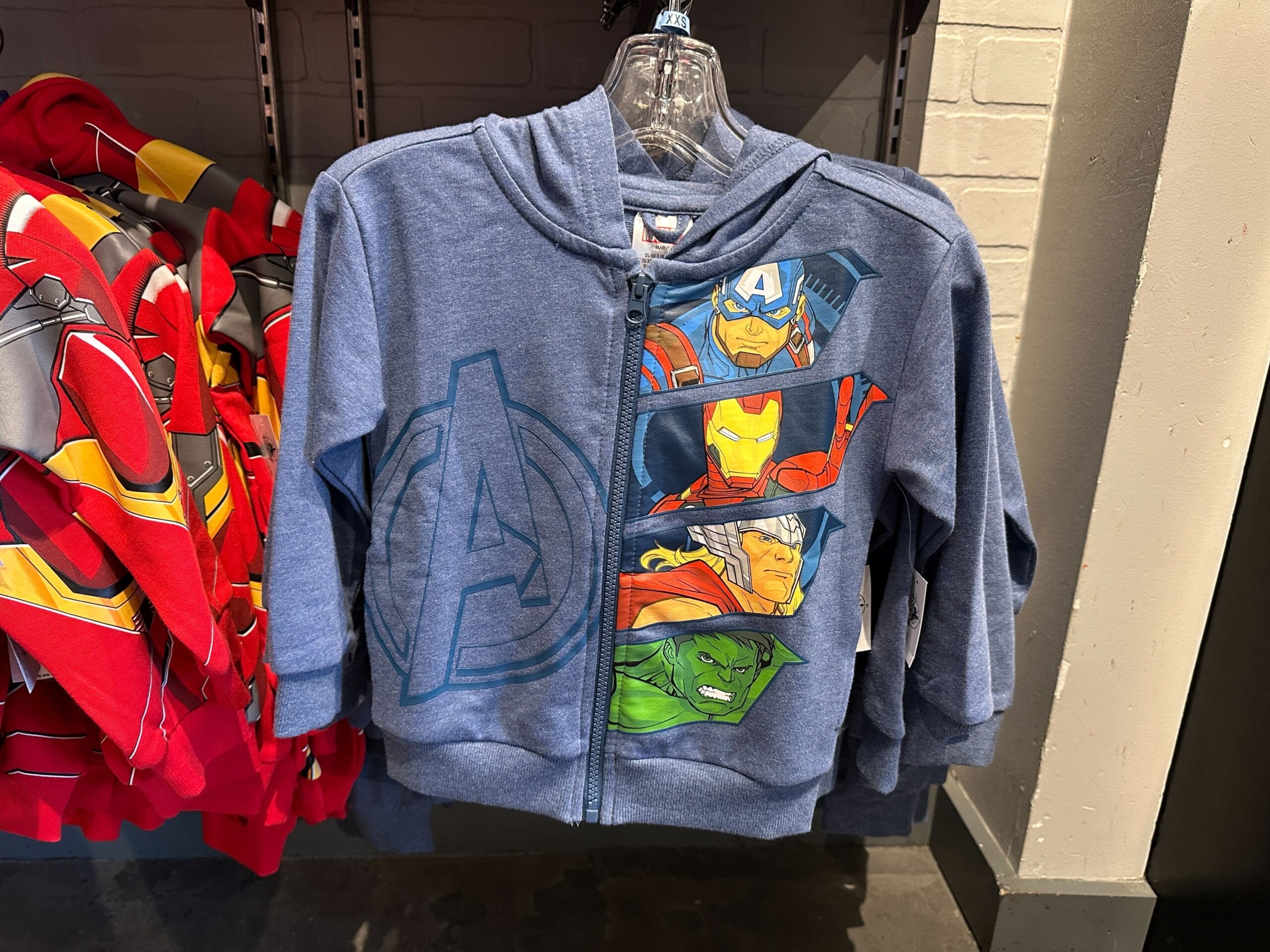 Youth Avengers Apparel: Blue hoodie with Captain America, Iron Man, Thor, and Hulk on the front, hanging on a store rack.