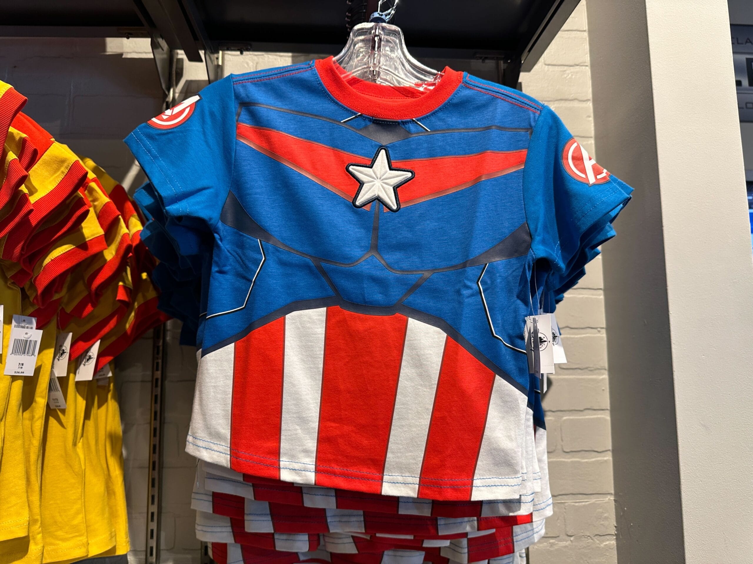 A Youth Avengers Apparel T-shirt styled like Captain America's costume hangs on a store rack.