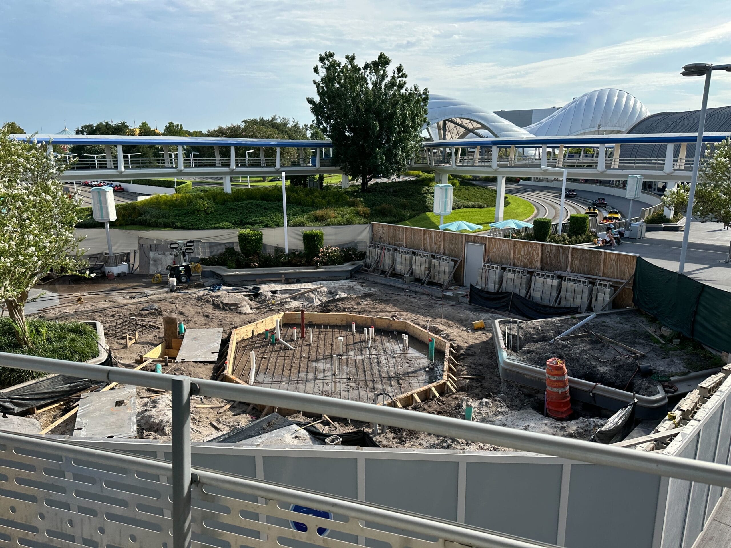 Construction site with dirt, barriers, and equipment near a monorail track and futuristic buildings in the background.