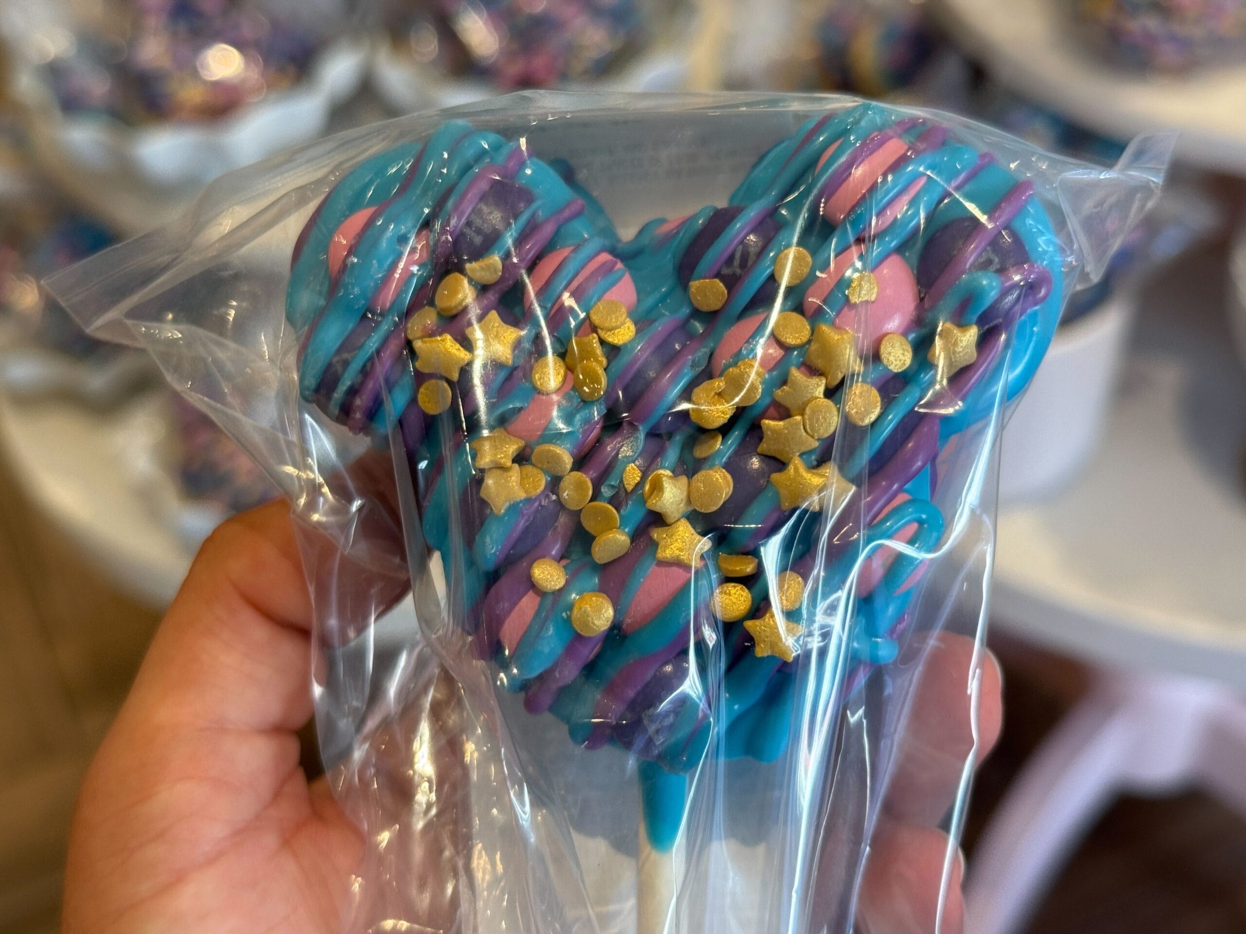 A heart-shaped treat with colorful icing and gold sprinkles, inspired by Disney Starlight Parade snacks, in a clear wrapper.