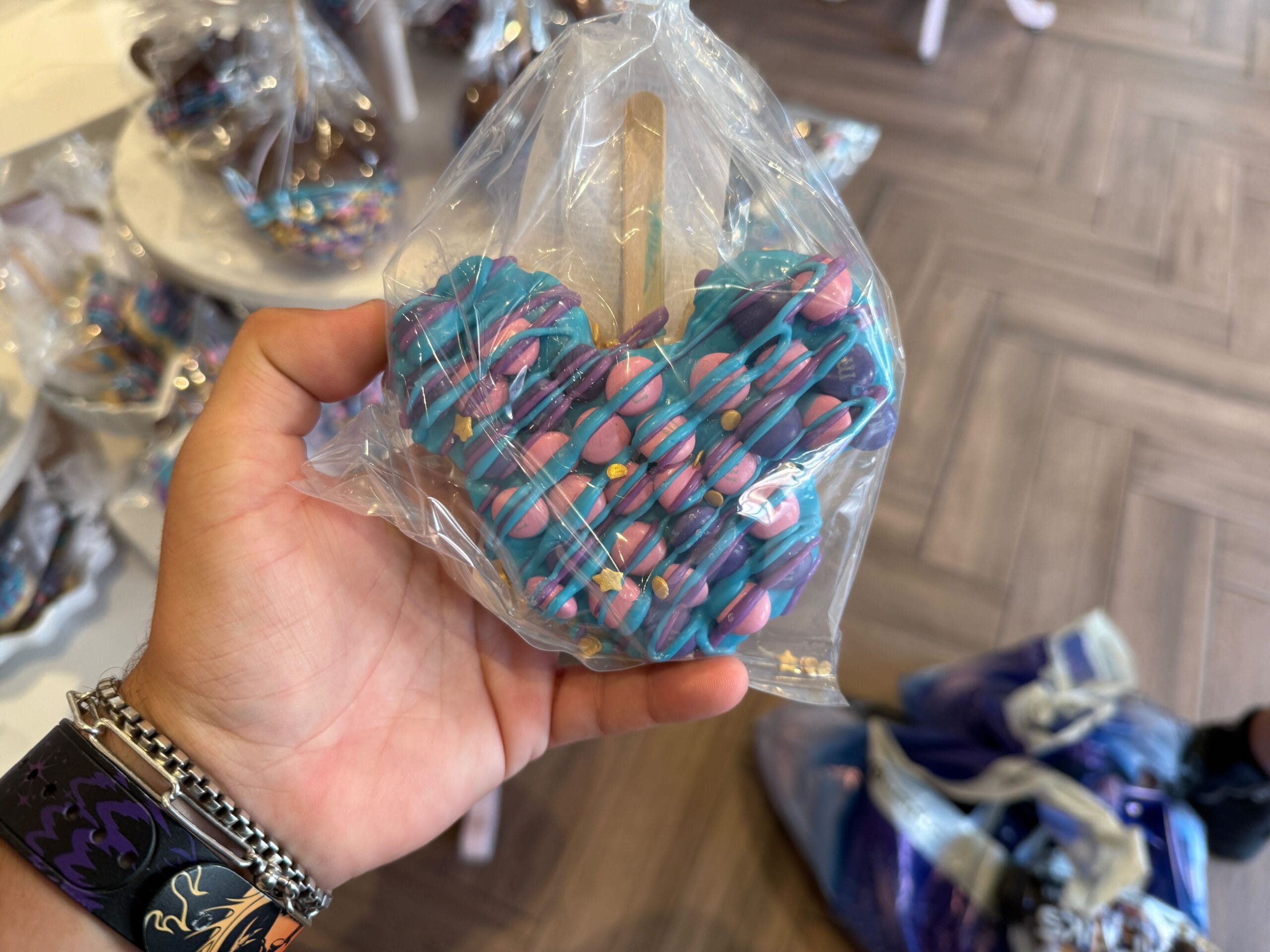 A hand holds a blue and pink drizzled Mickey Mouse treat—a sweet Disney Starlight Parade snack—in a clear plastic bag.