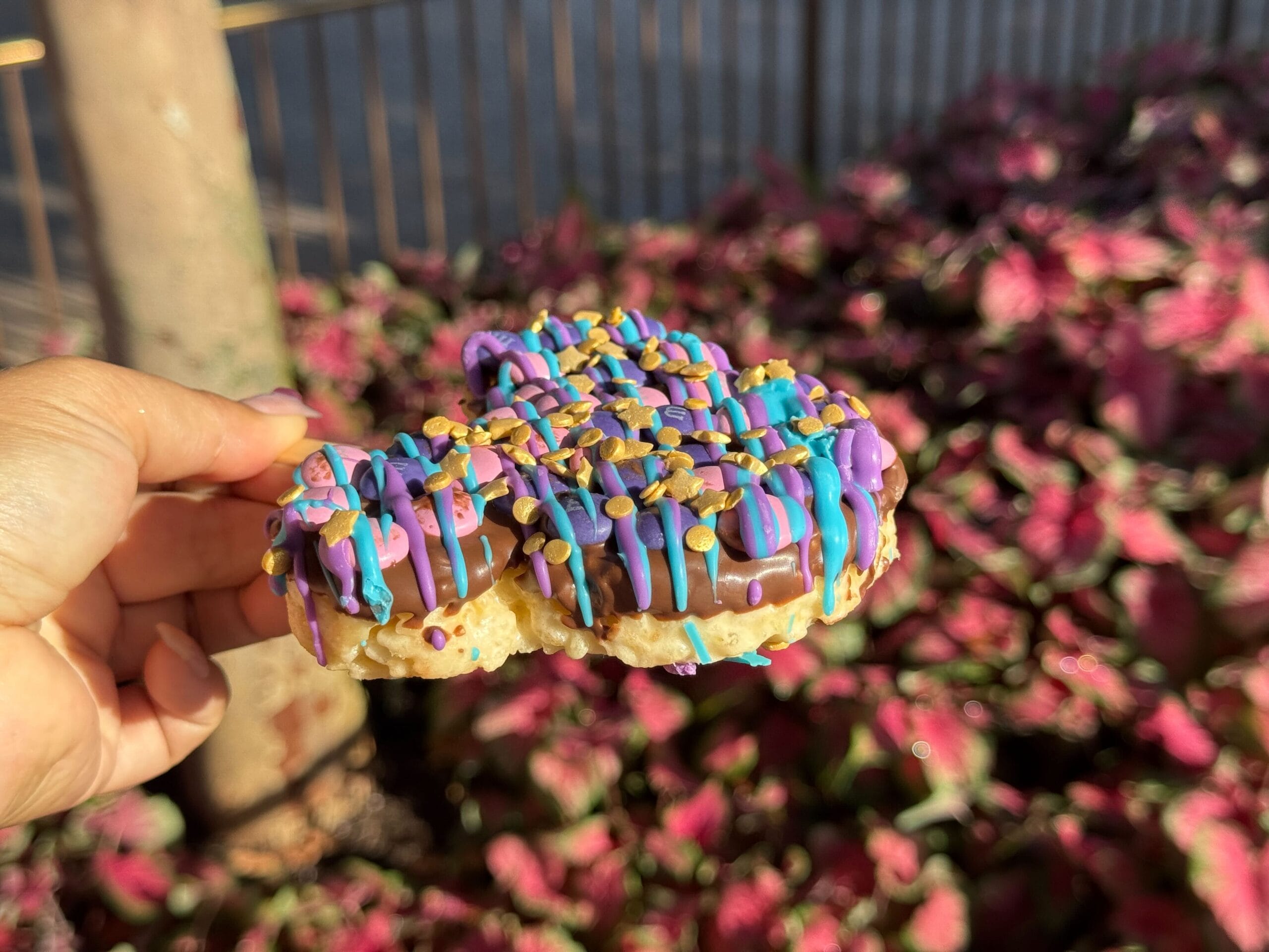 A hand holds a Mickey-shaped rice treat with colorful icing and sprinkles, a favorite snack at Magic Kingdom.