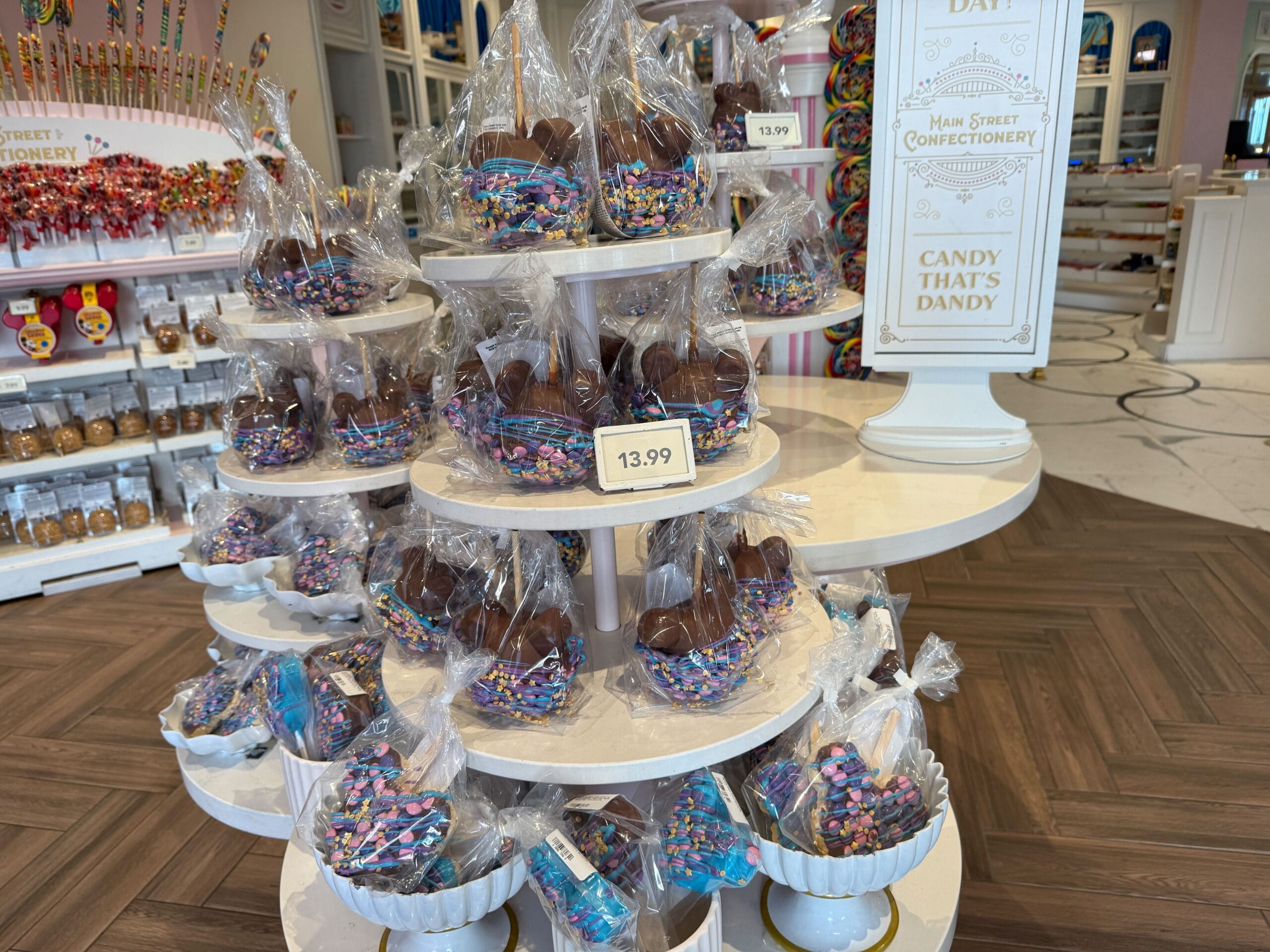 New Disney Parade Treats Chocolate-covered treats in clear bags with sprinkles, perfect Magic Kingdom snacks, displayed on a white tiered stand.