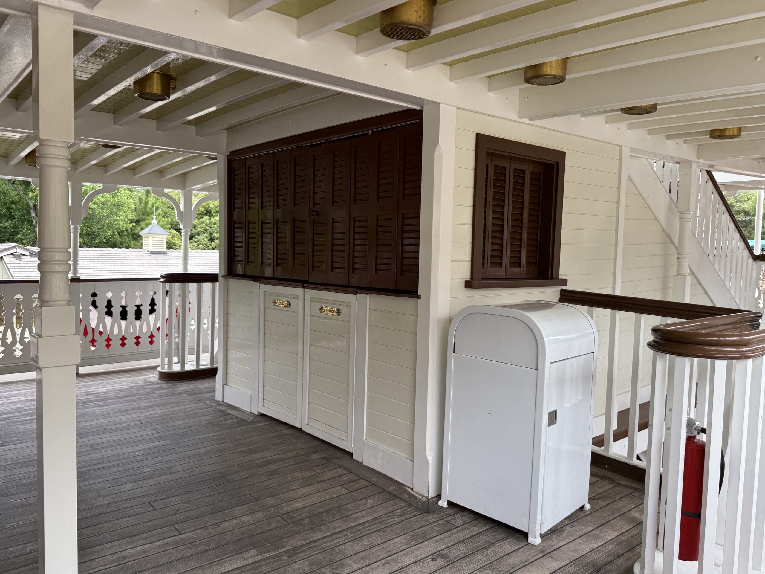 Covered deck area with white railings, brown shuttered window, and wooden floors like the Liberty Square Riverboat.