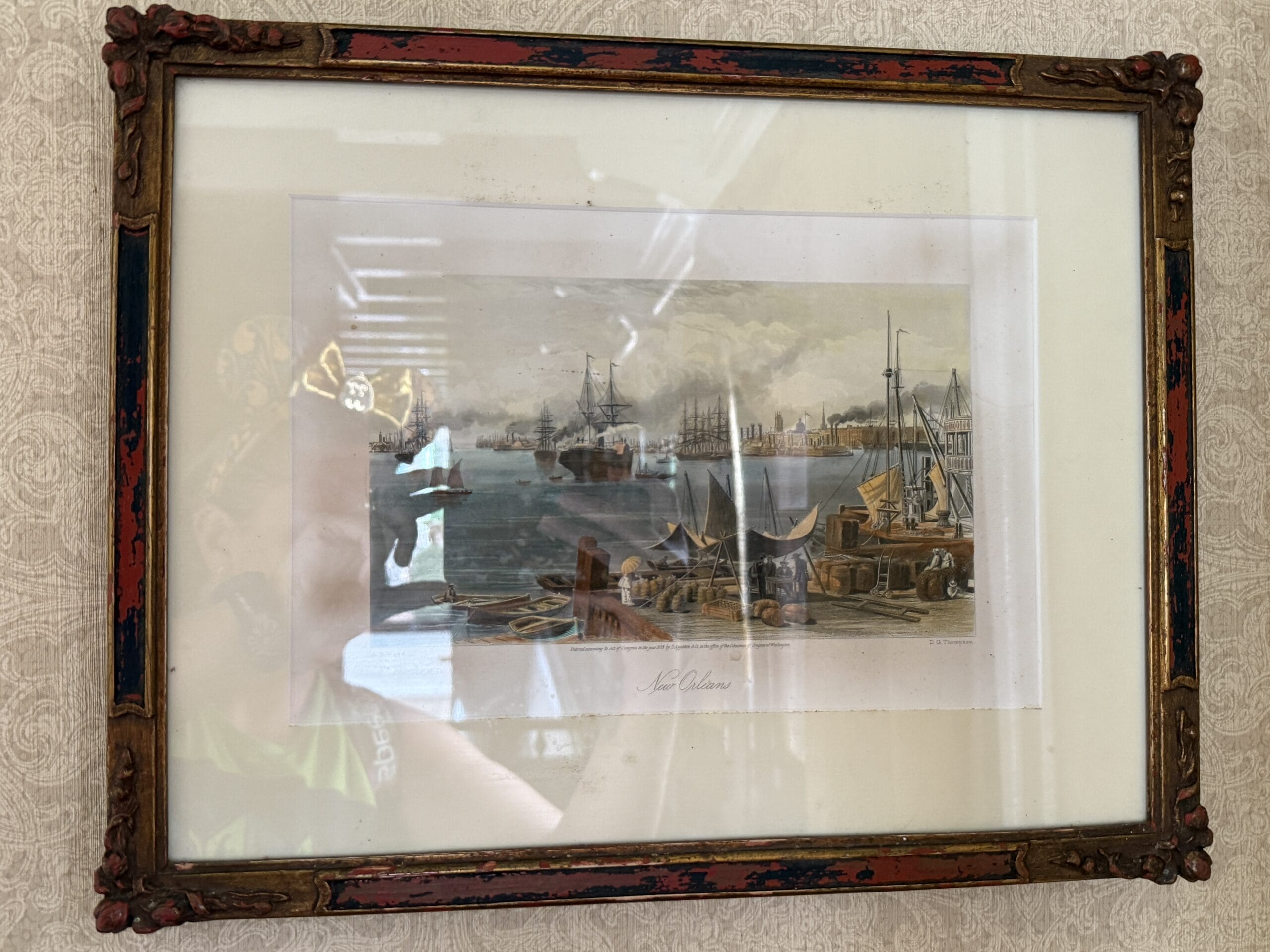 Framed painting of a busy 19th-century harbor scene, reminiscent of the Liberty Square Riverboat, on a patterned wall.