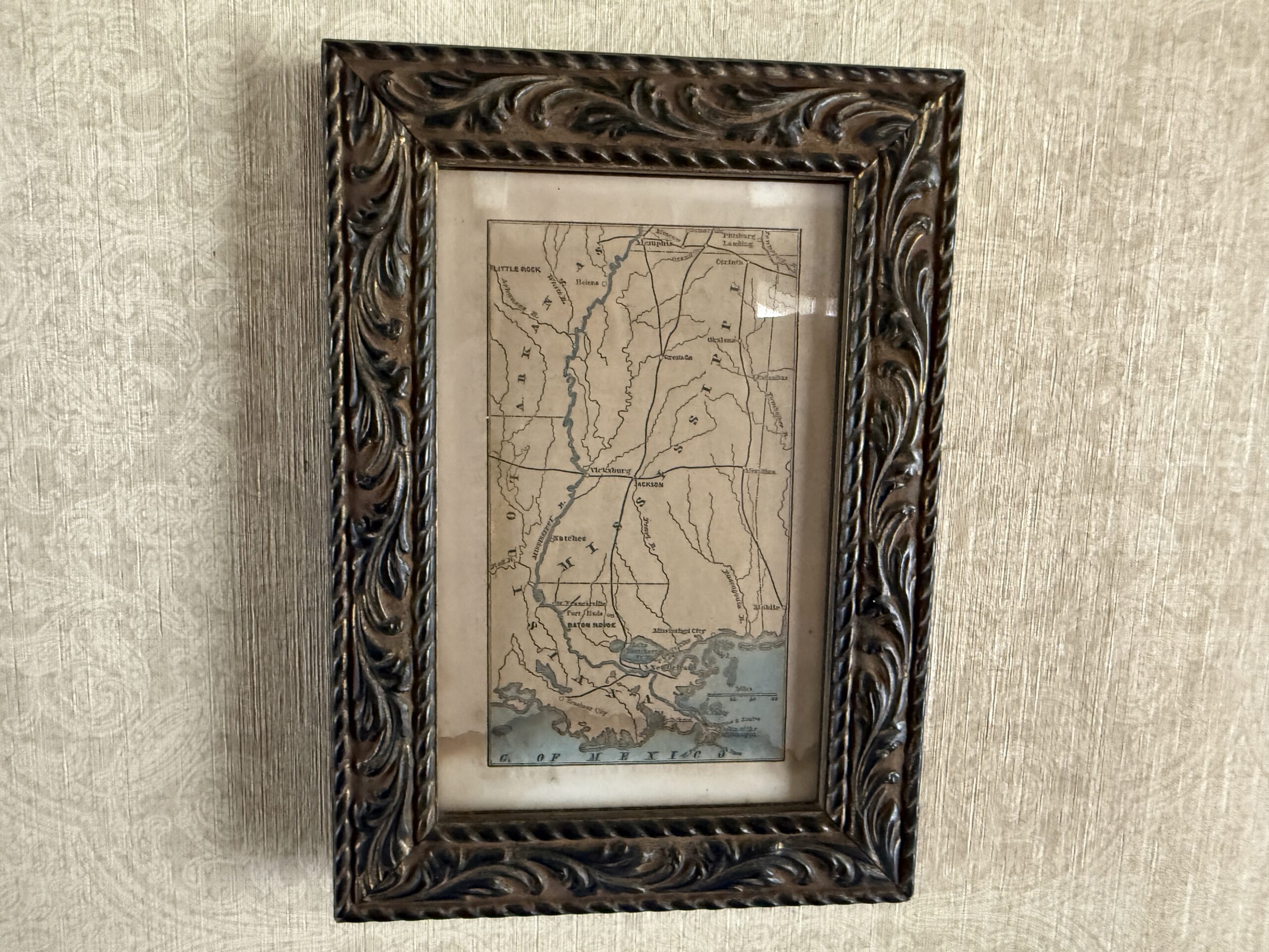 Framed vintage map with ornate brown border, featuring the Magic Kingdom, hangs on a textured beige wall.