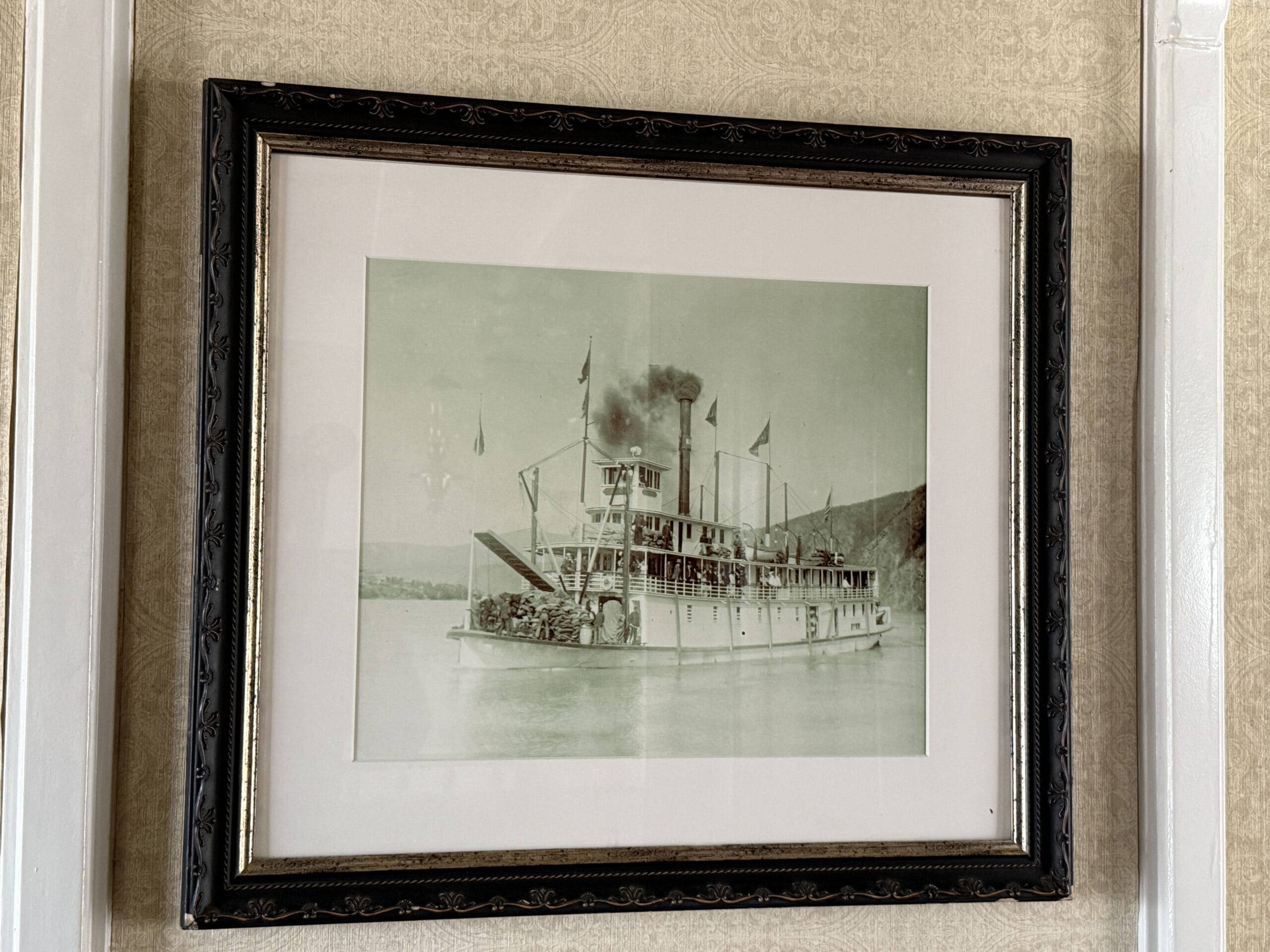Framed vintage photograph of the Liberty Square Riverboat on the water, hanging on a patterned wall in Magic Kingdom.