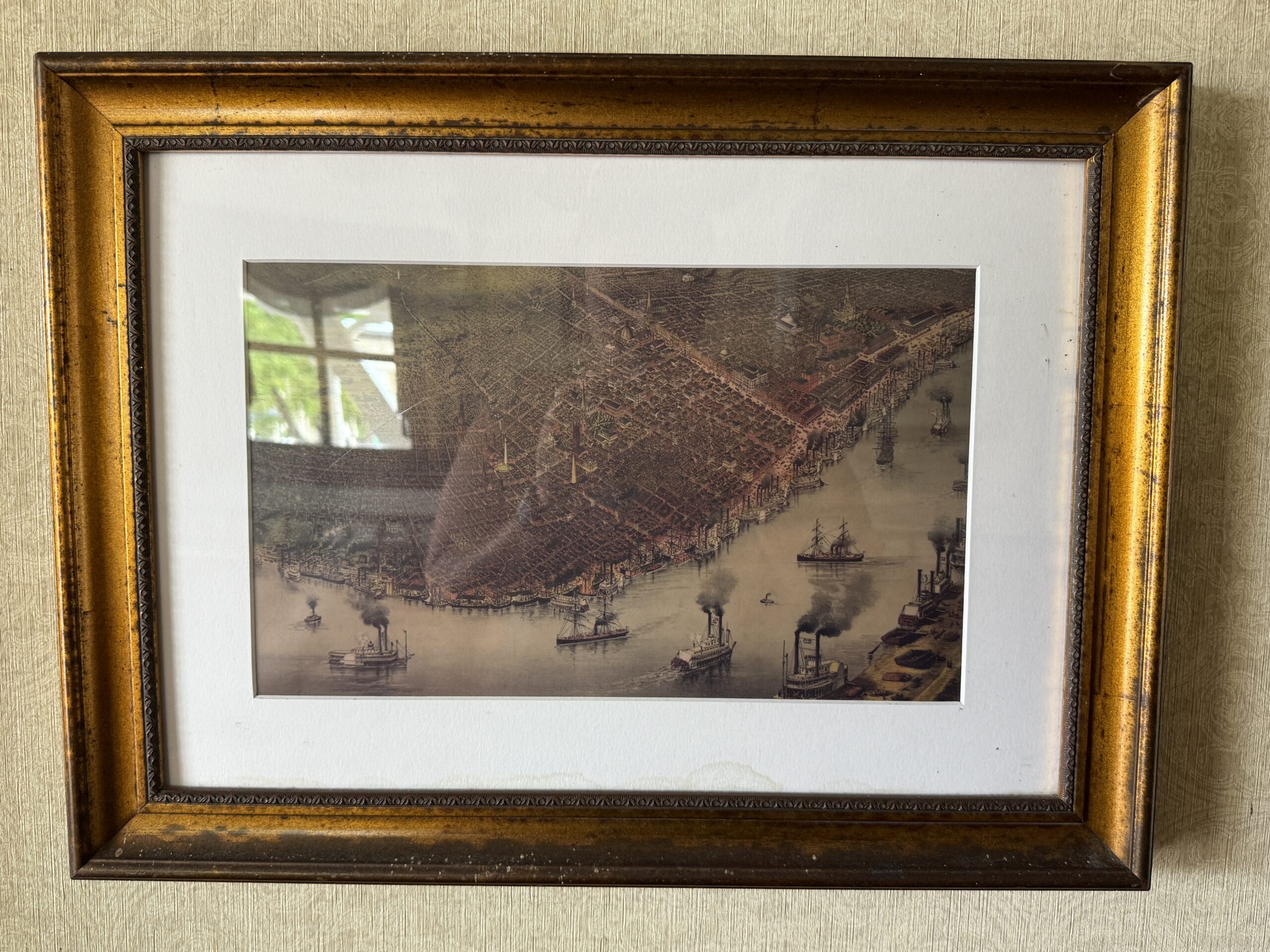 Framed vintage map of a city harbor with steamboats, reminiscent of the Liberty Square Riverboat, on a textured wall.
