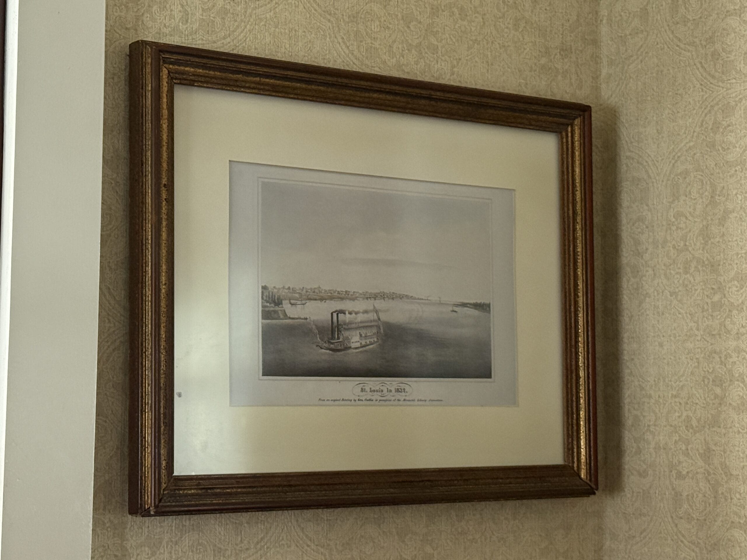 Framed black-and-white print of the Liberty Square Riverboat hangs on a patterned beige wall.