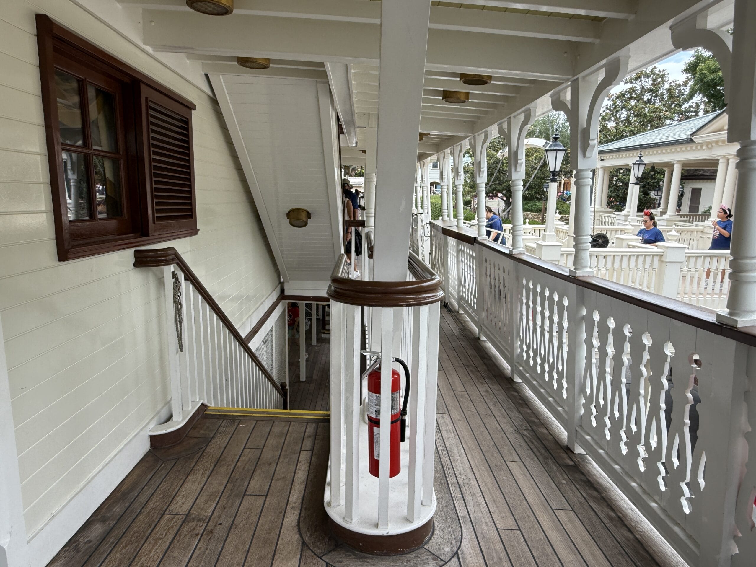 Wooden deck with white railings, stairs, and red fire extinguisher at Liberty Square Riverboat in Magic Kingdom.