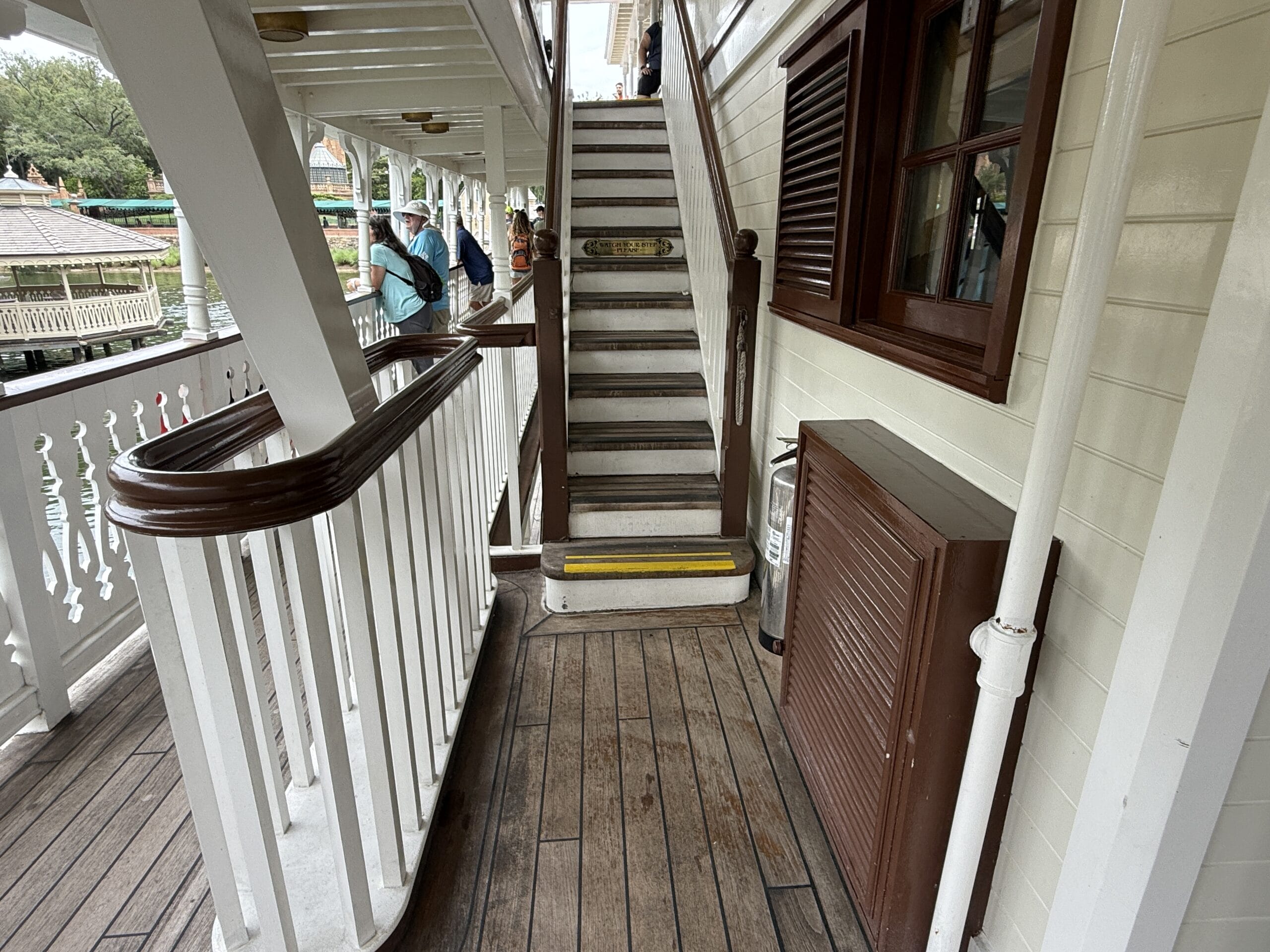 Wooden stairs with a yellow caution strip on the Liberty Square Riverboat, surrounded by white railings and brown trim.