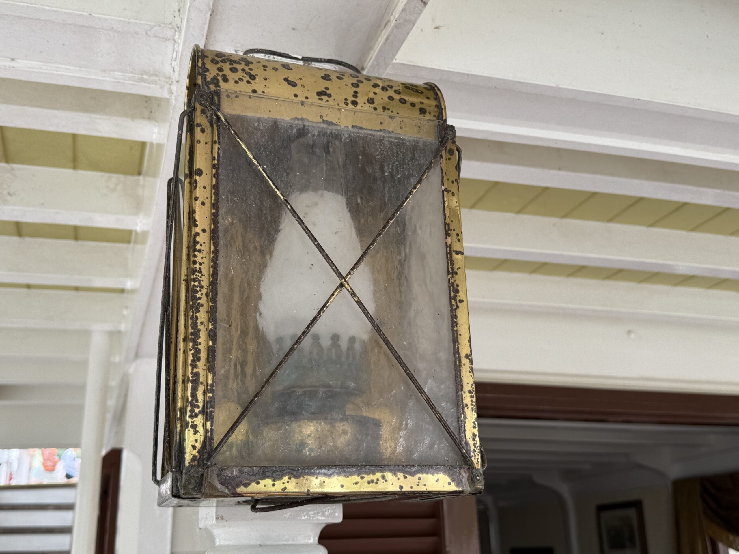 Close-up of an old brass lantern with frosted glass on a white beam, seen near Liberty Square Riverboat in Magic Kingdom.