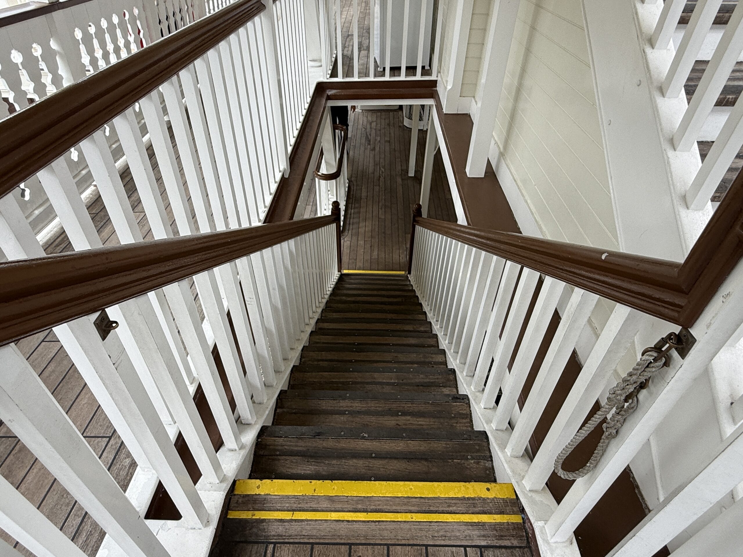 Wooden staircase with white railings and yellow safety lines, leading to the Liberty Square Riverboat at Magic Kingdom.