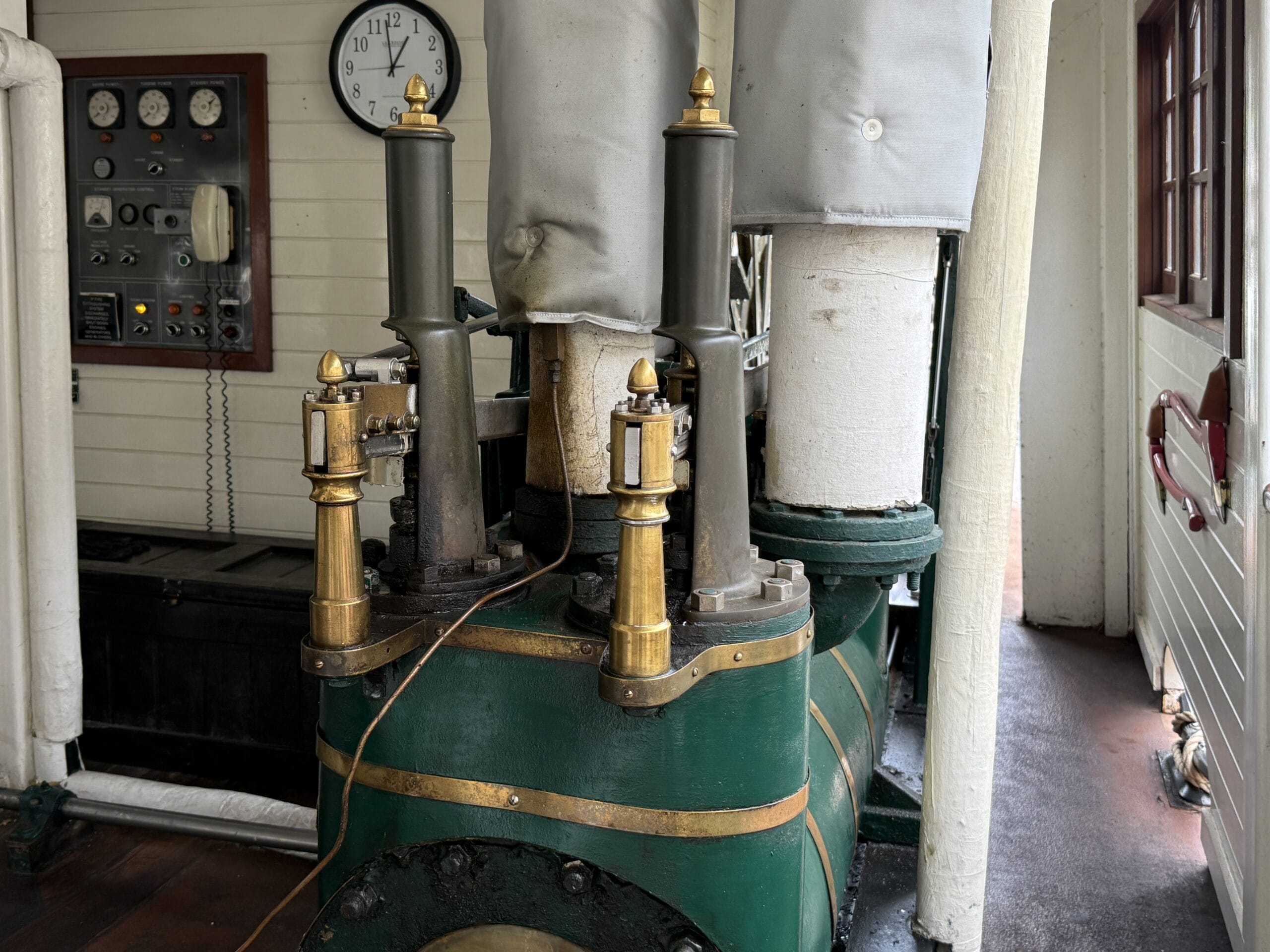 Green and brass steam engine inside a room with gauges, pipes, and clock, like on the Magic Kingdom Liberty Square Riverboat.