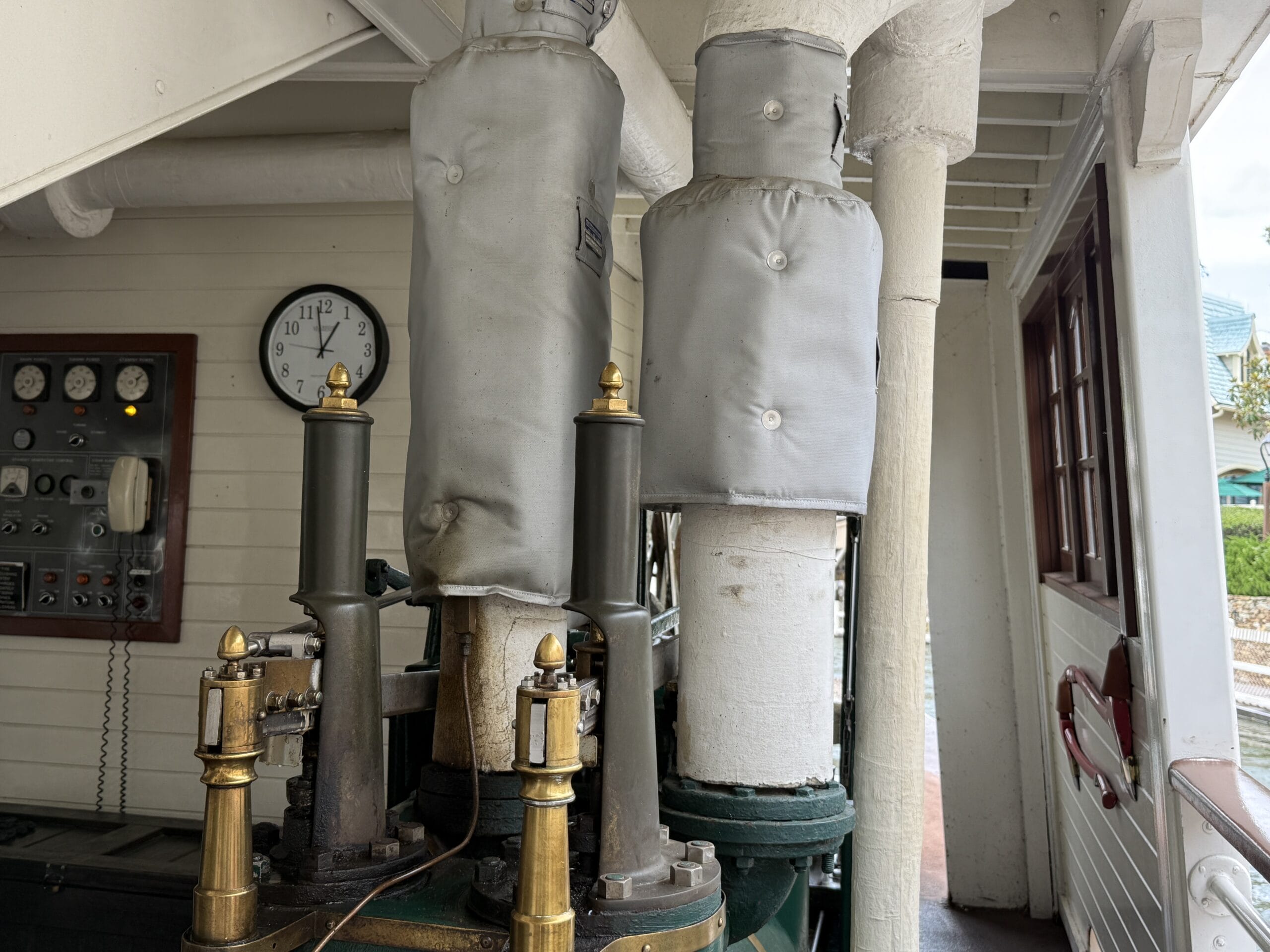 Close-up of insulated steam pipes aboard the Liberty Square Riverboat, with a wall clock and control panel in the background.