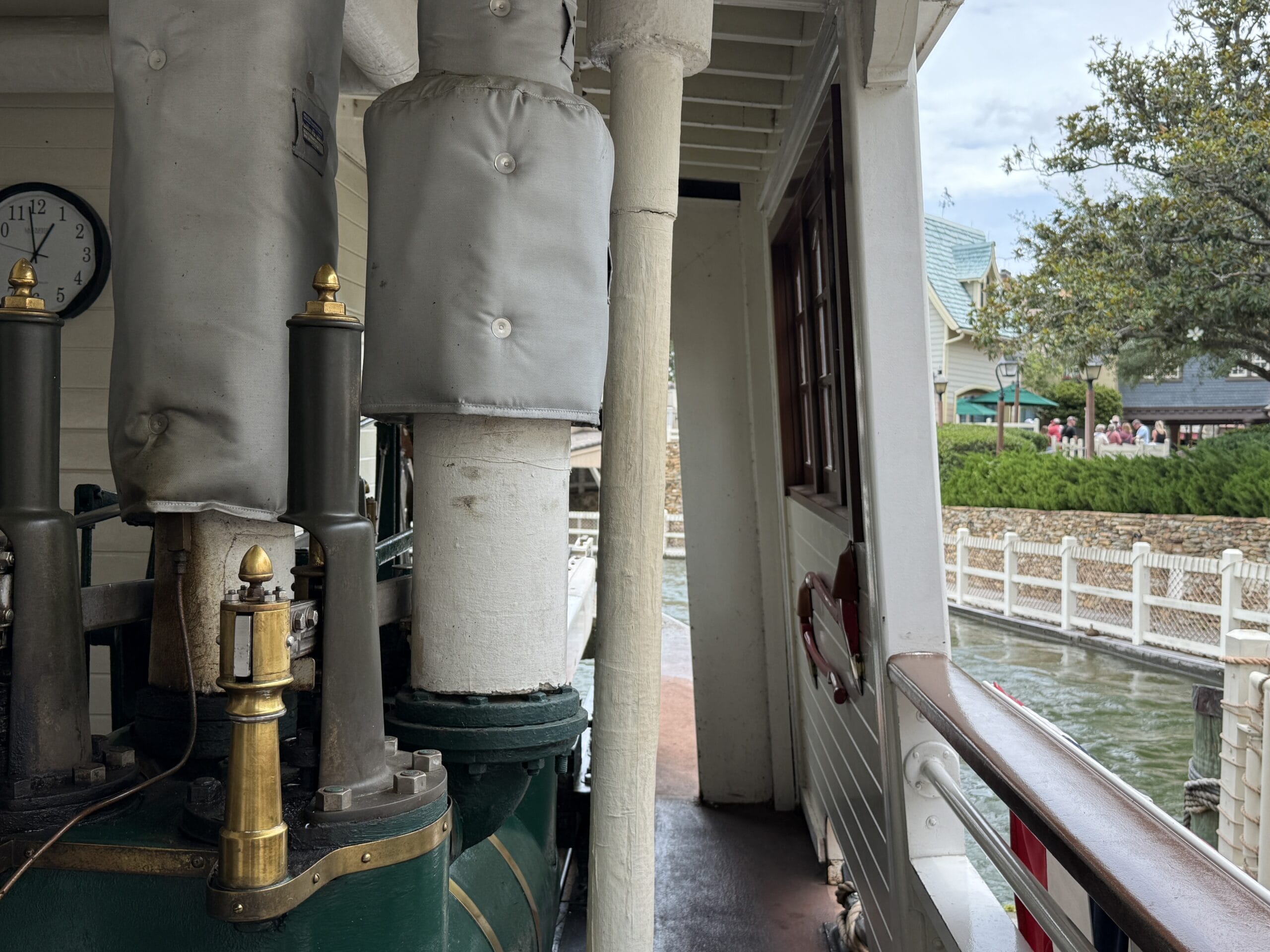 View from the Liberty Square Riverboat deck, showing steam pipes, railing, and Magic Kingdom’s riverside theme park in the background.