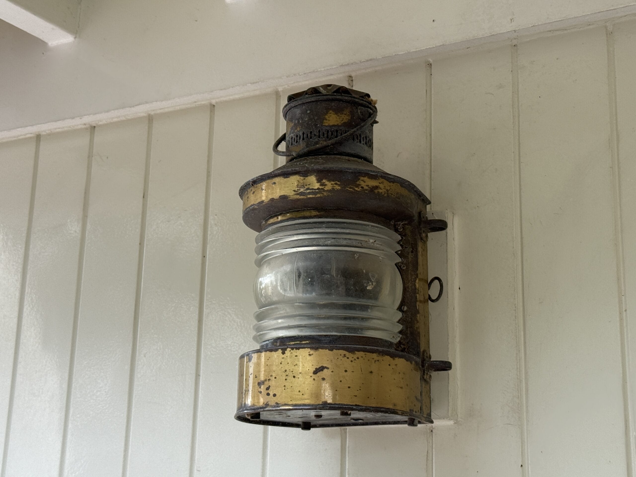 An old brass lantern with a glass center hangs on a white wall near the Liberty Square Riverboat.
