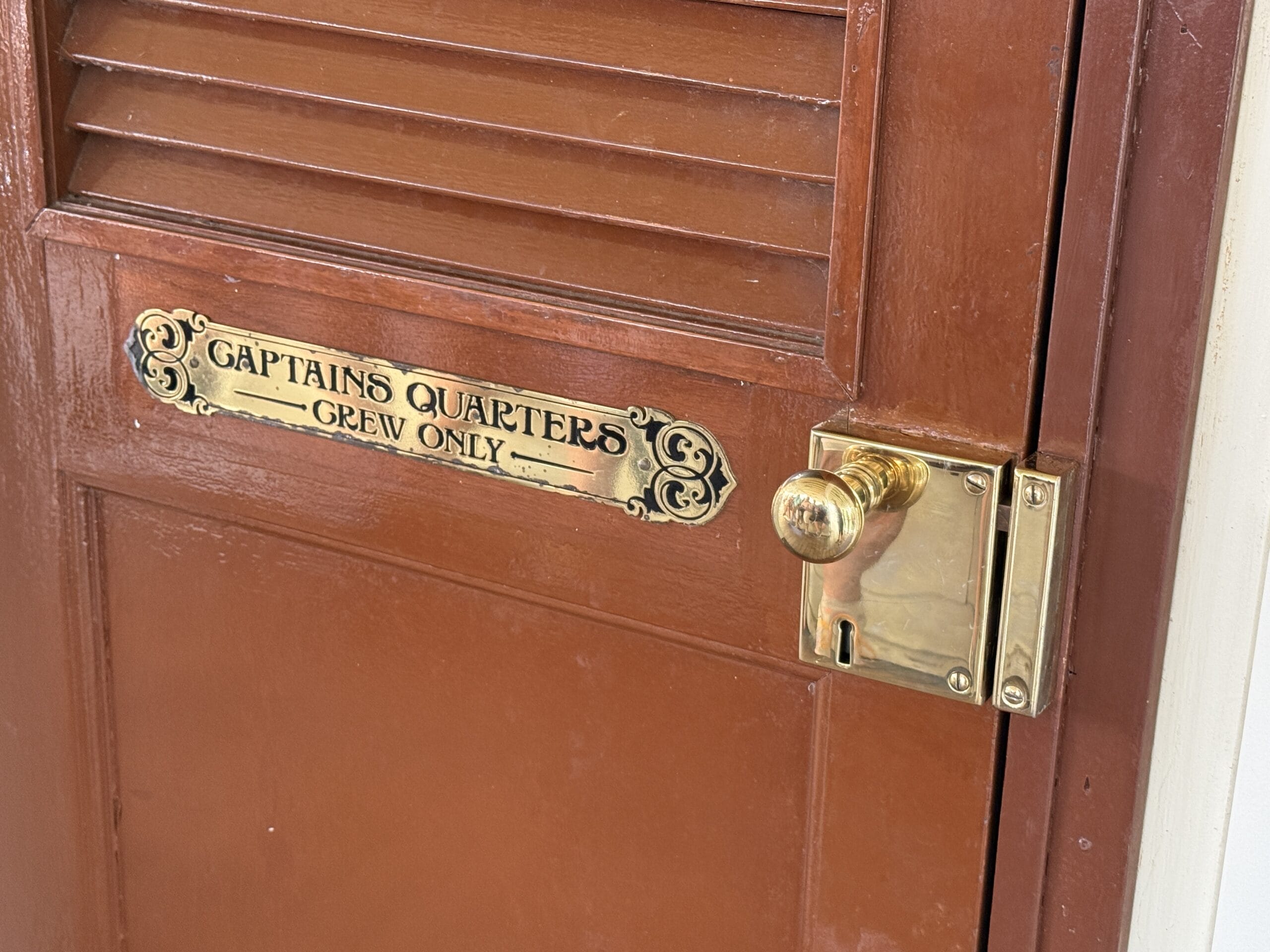 Brown door with brass sign reading "CAPTAIN'S QUARTERS CREW ONLY" on the Liberty Square Riverboat in Magic Kingdom.