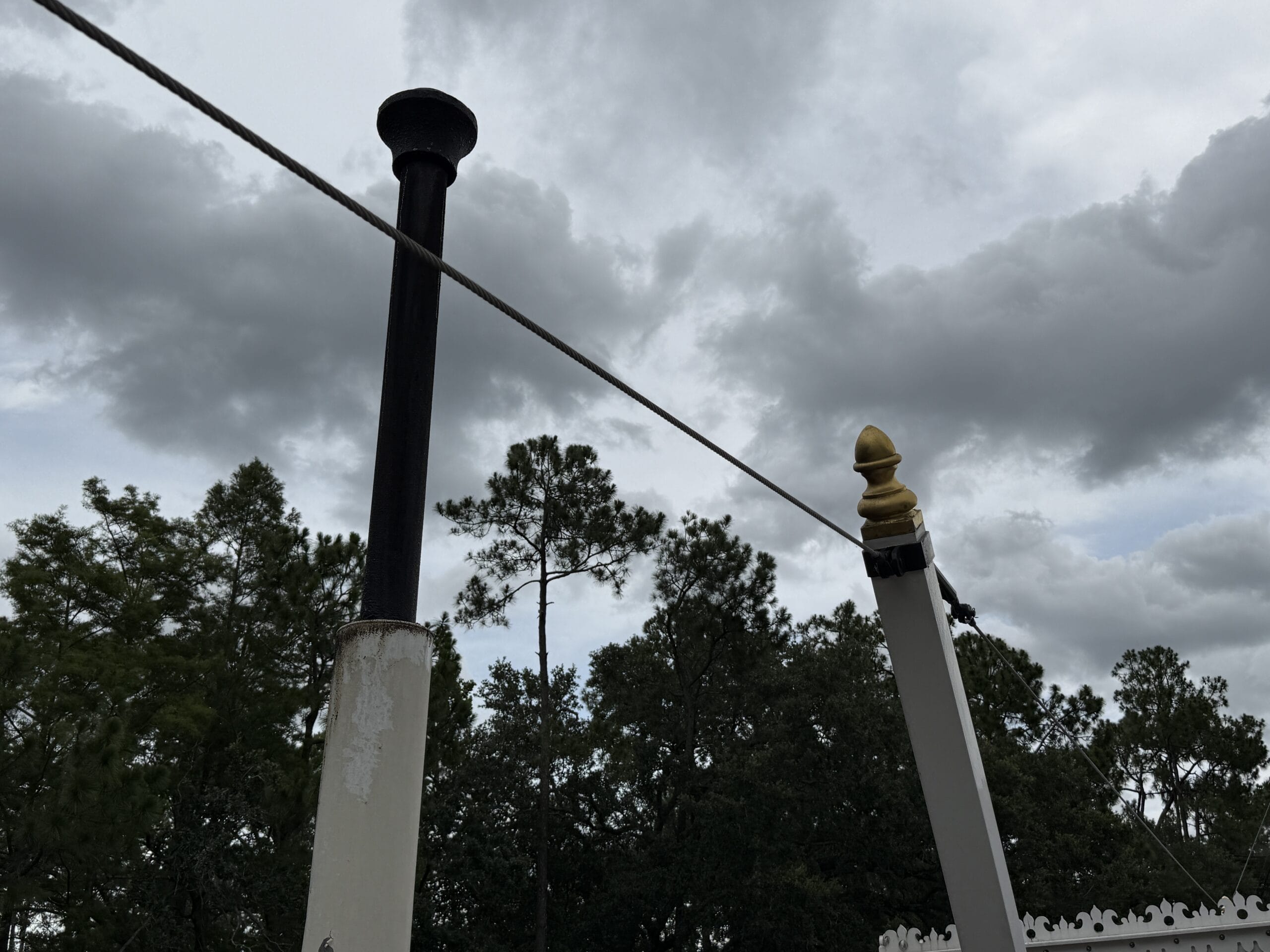 A steamship smokestack and pole rise against a cloudy sky near the Liberty Square Riverboat in Magic Kingdom.