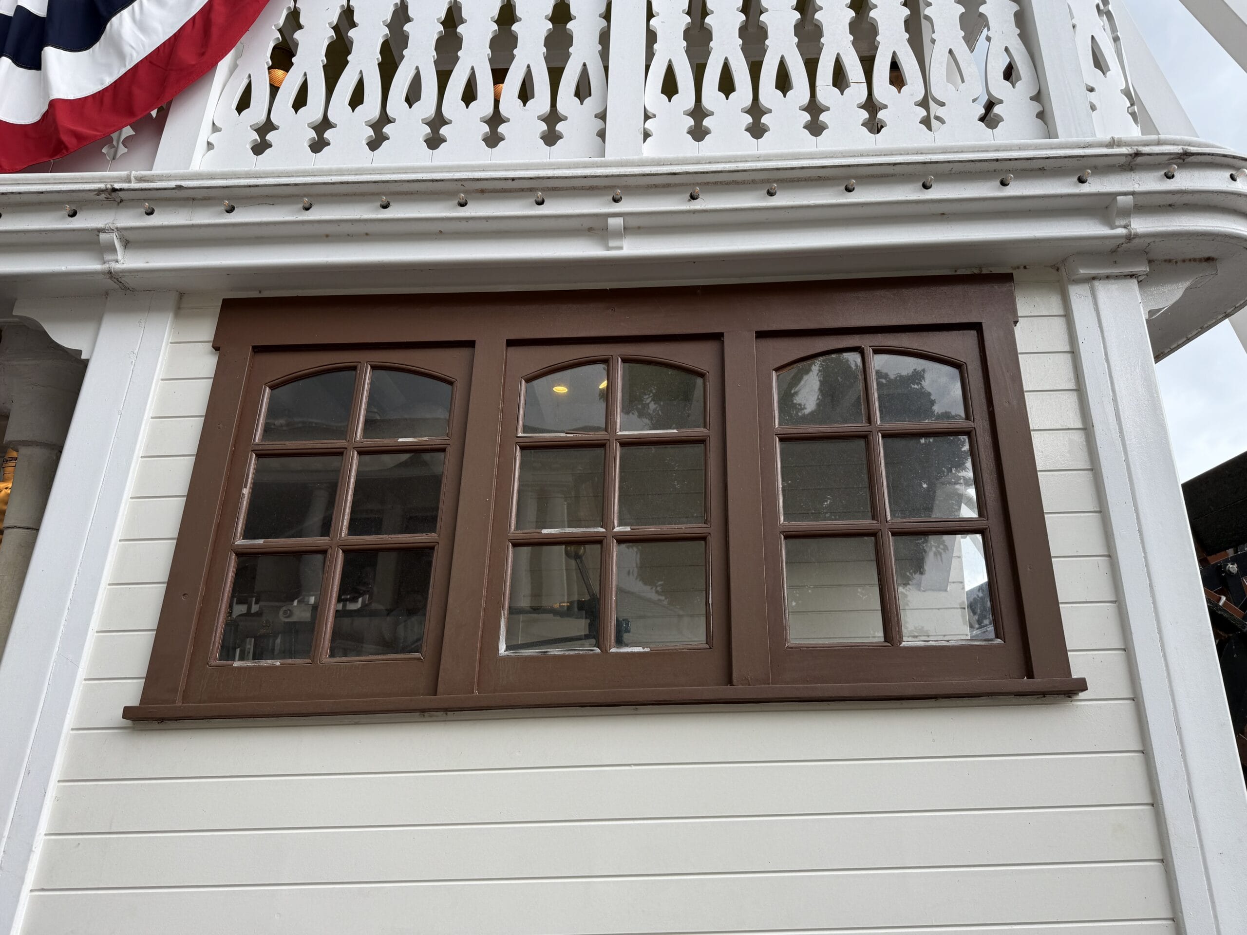 Three brown-framed windows on a white wooden wall near the Liberty Square Riverboat, with red, white, and blue bunting above.