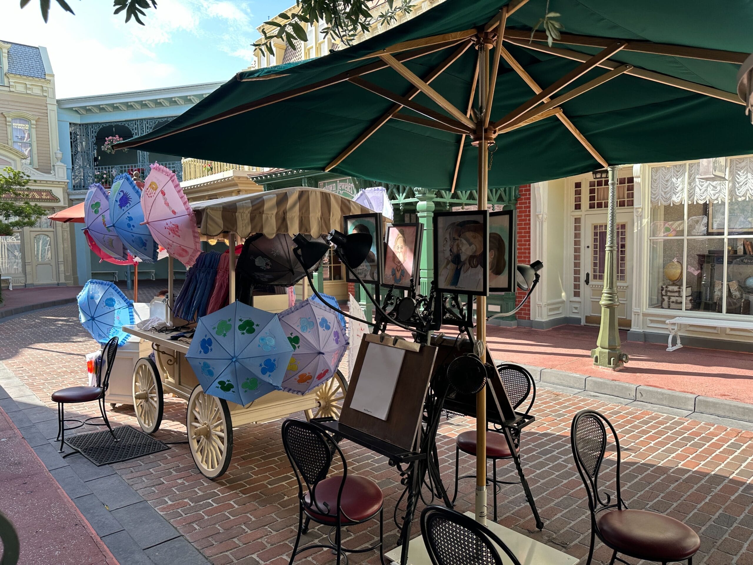 Outdoor umbrella cart with colorful umbrellas for sale, surrounded by café chairs and tables on a brick street.