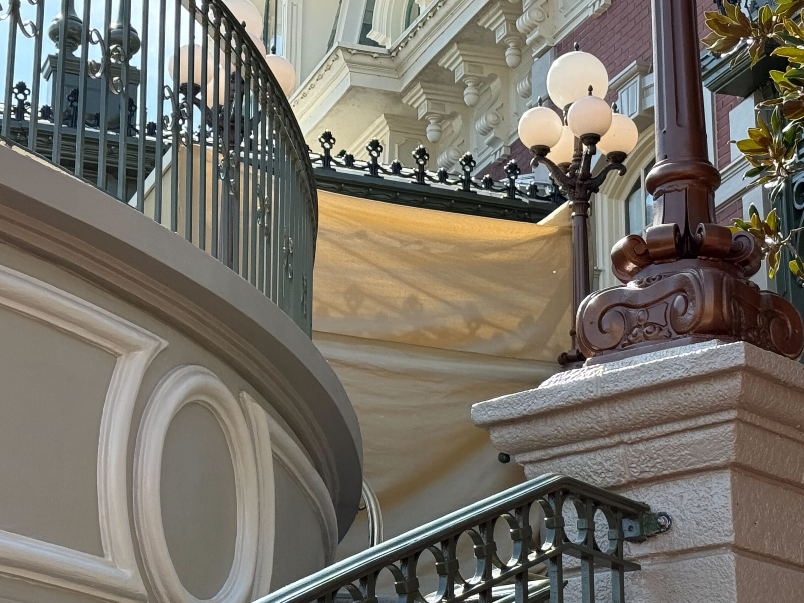 Iron railing and a stairway next to a modern lamppost, with beige construction tarps behind them.