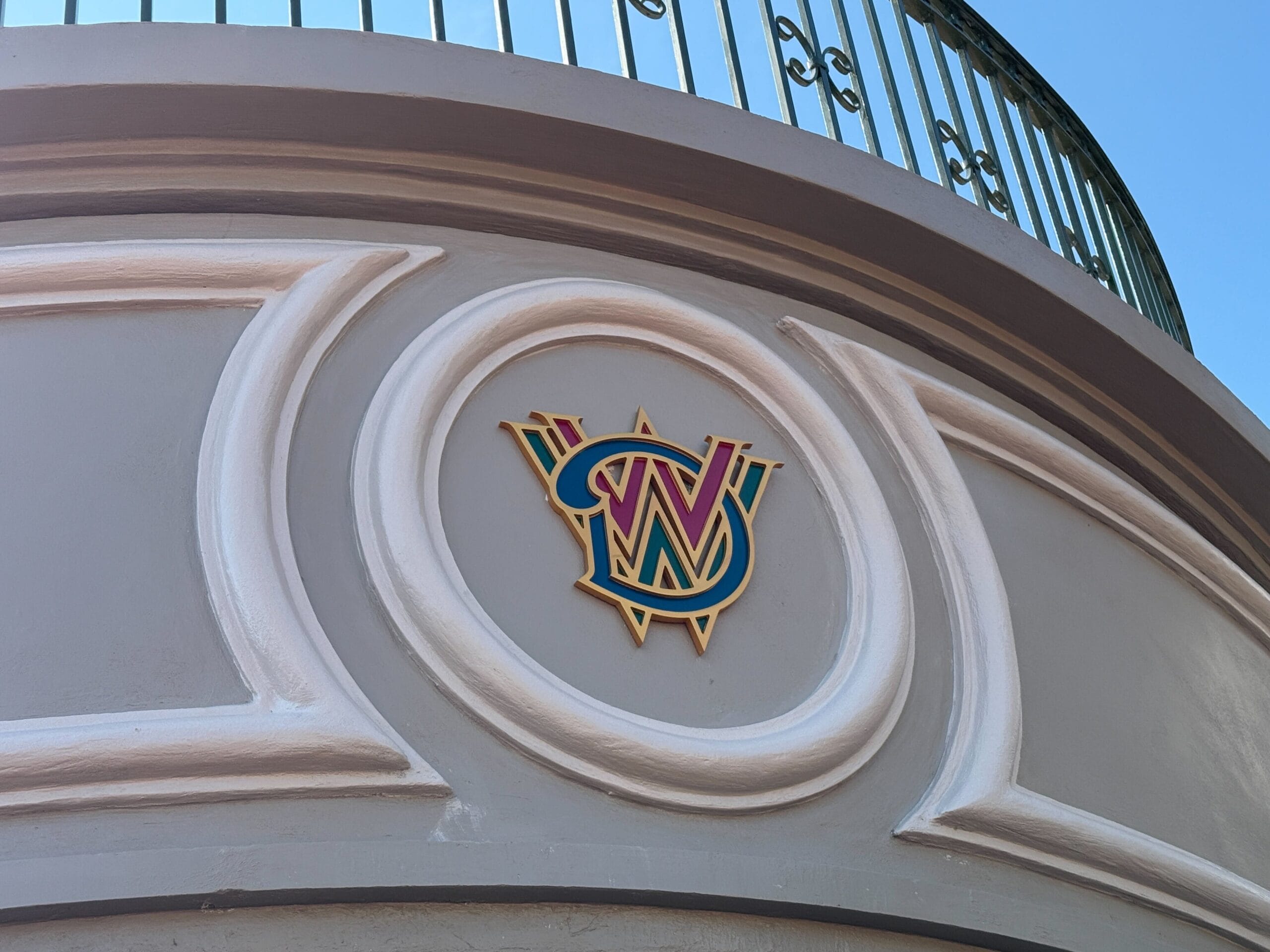 Colorful "W" and "D" emblem on a gray wall under a curved balcony with a metal railing against blue sky.