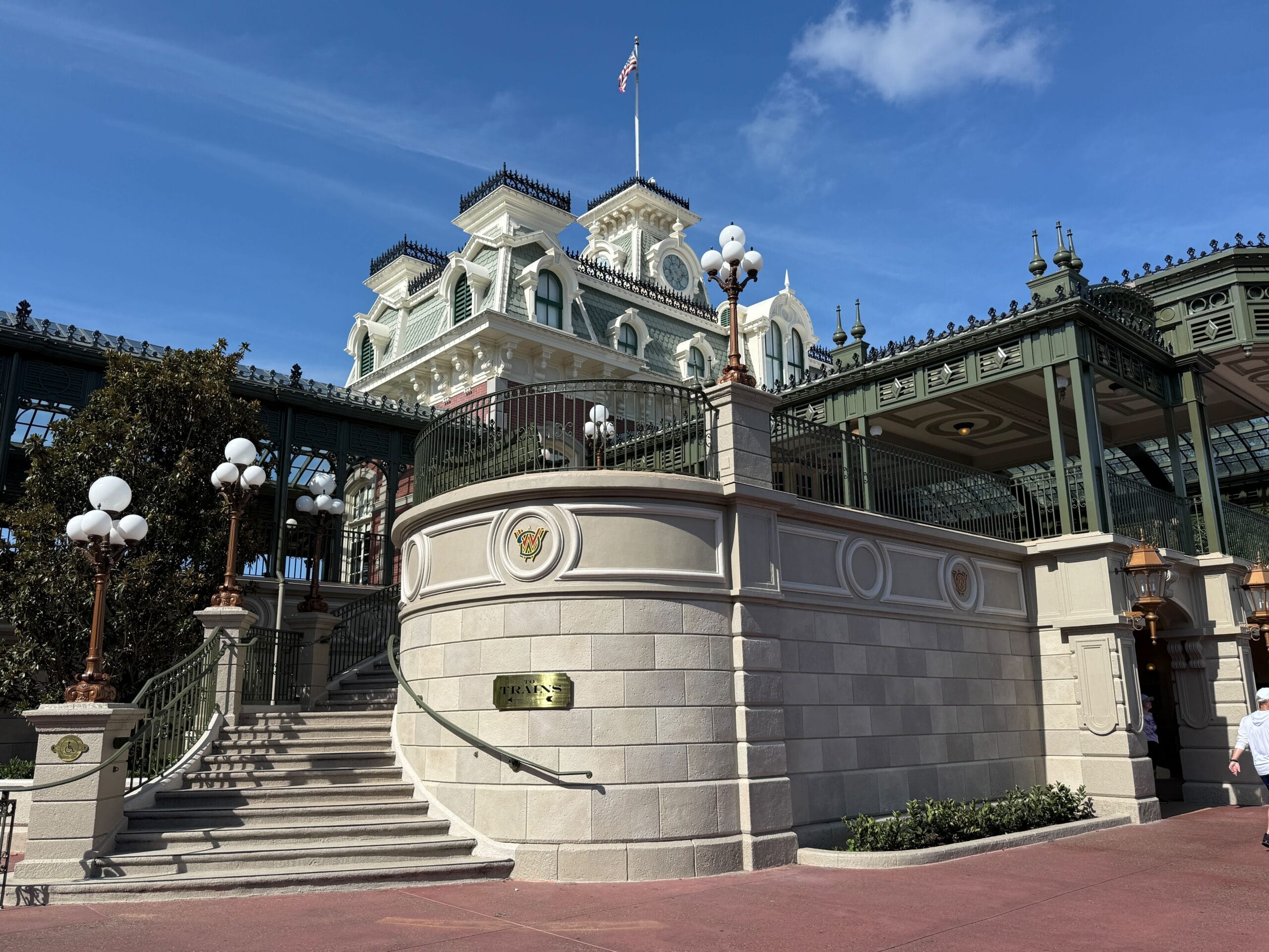 A bright, sunny view of the Magic Kingdom entrance with Victorian-style architecture and white lamp posts.
