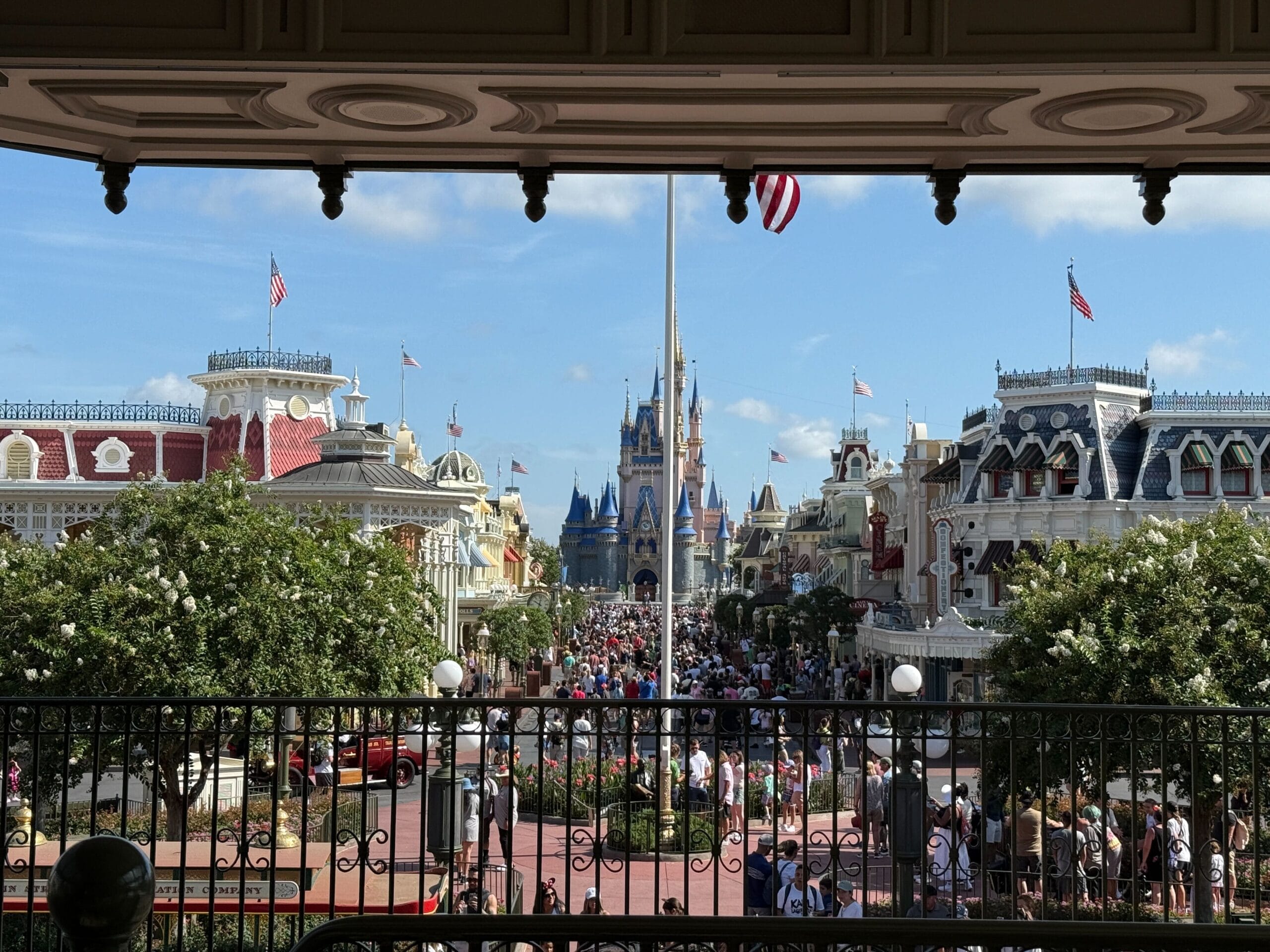 View of a crowded Main Street in a Disney park, with Cinderella Castle in the distance under a blue sky.