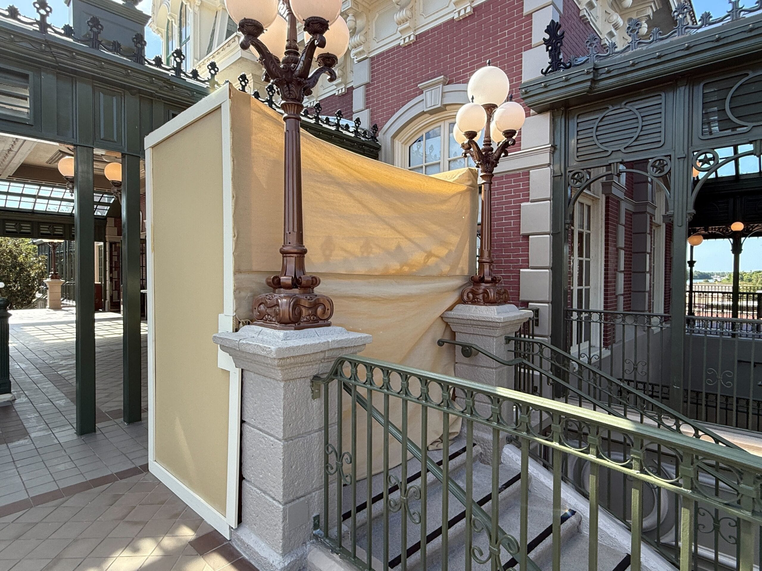 A staircase is blocked off with beige construction tarps and surrounded by green metal railings and vintage lamps.
