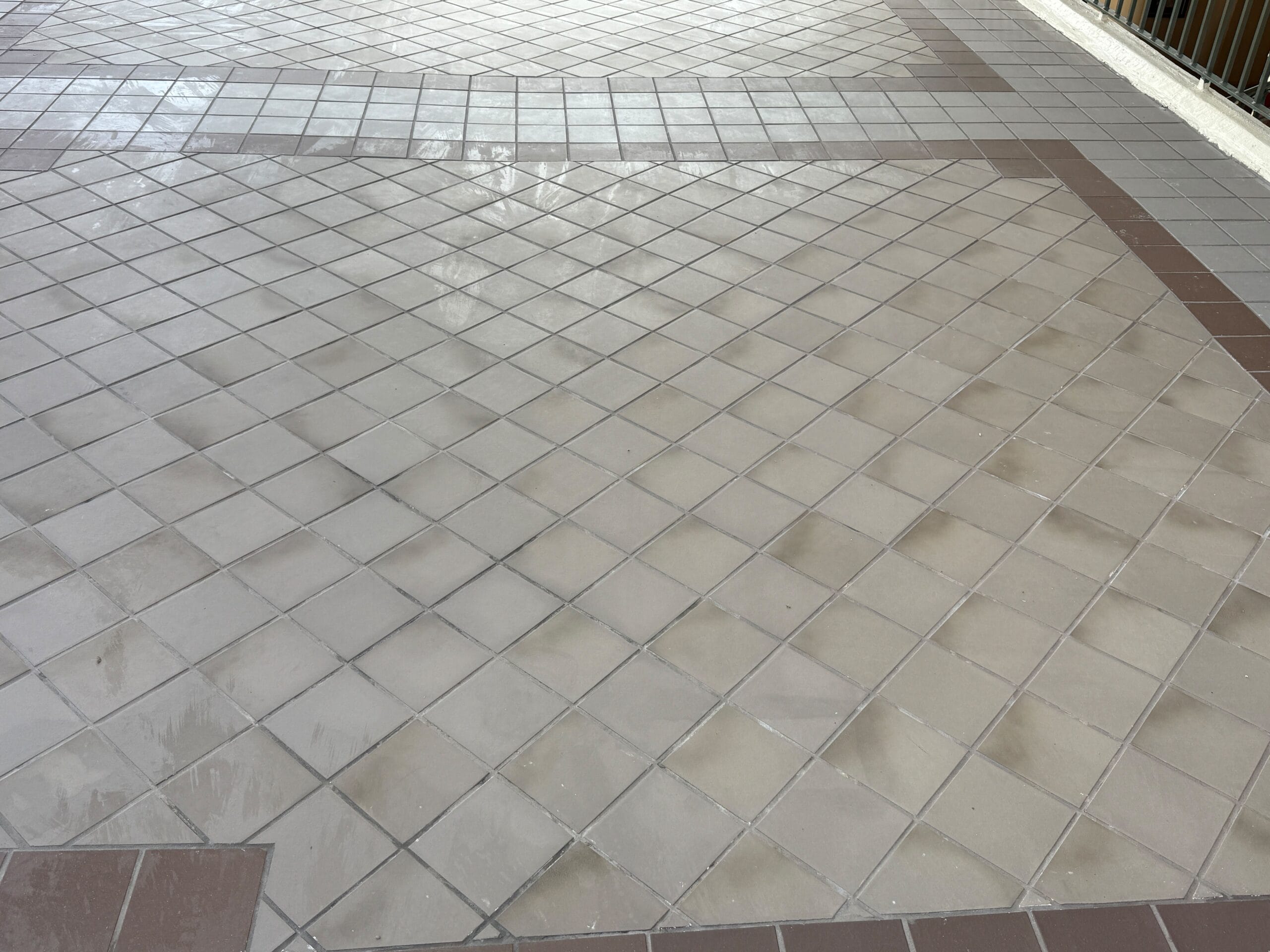 A tiled floor with beige square tiles bordered by brown tiles, appearing wet in some areas.