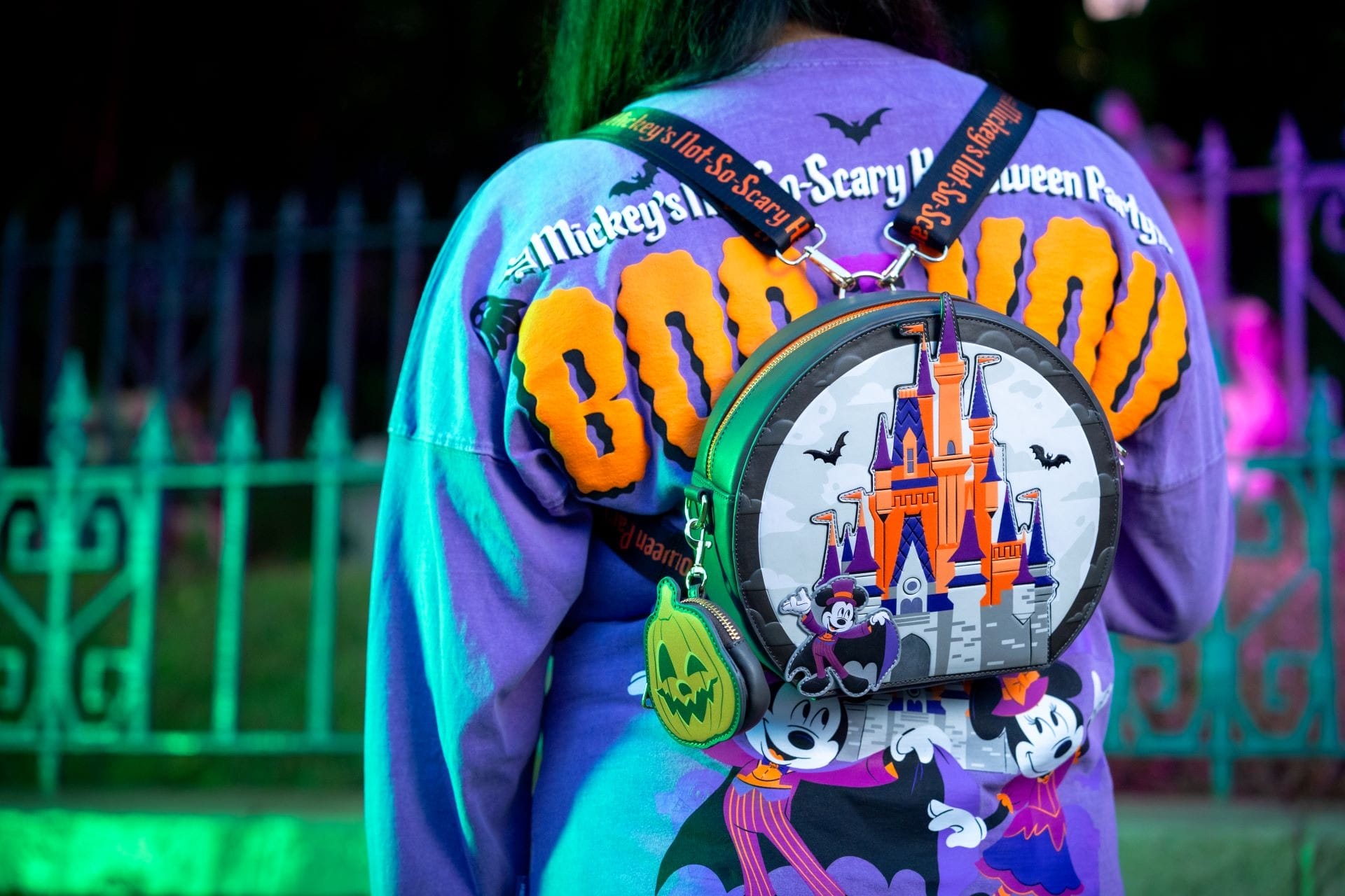 Person wearing a purple "BOO TO YOU!" shirt with Disney Halloween Merchandise: a Mickey Mouse castle and bats backpack.