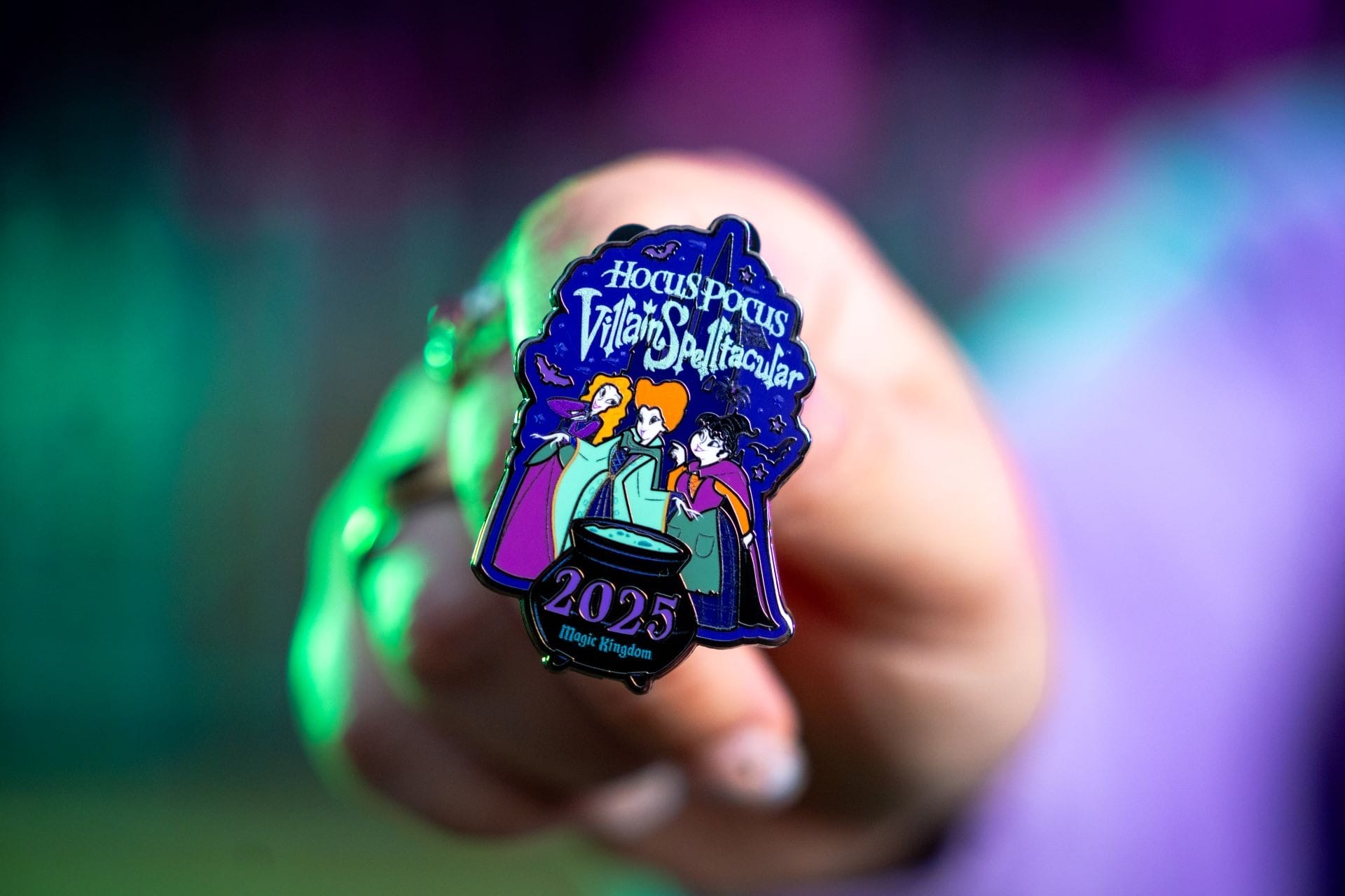 A hand holds a “Hocus Pocus Villain Spelltacular 2025” pin—perfect Disney merchandise for Halloween collectors.