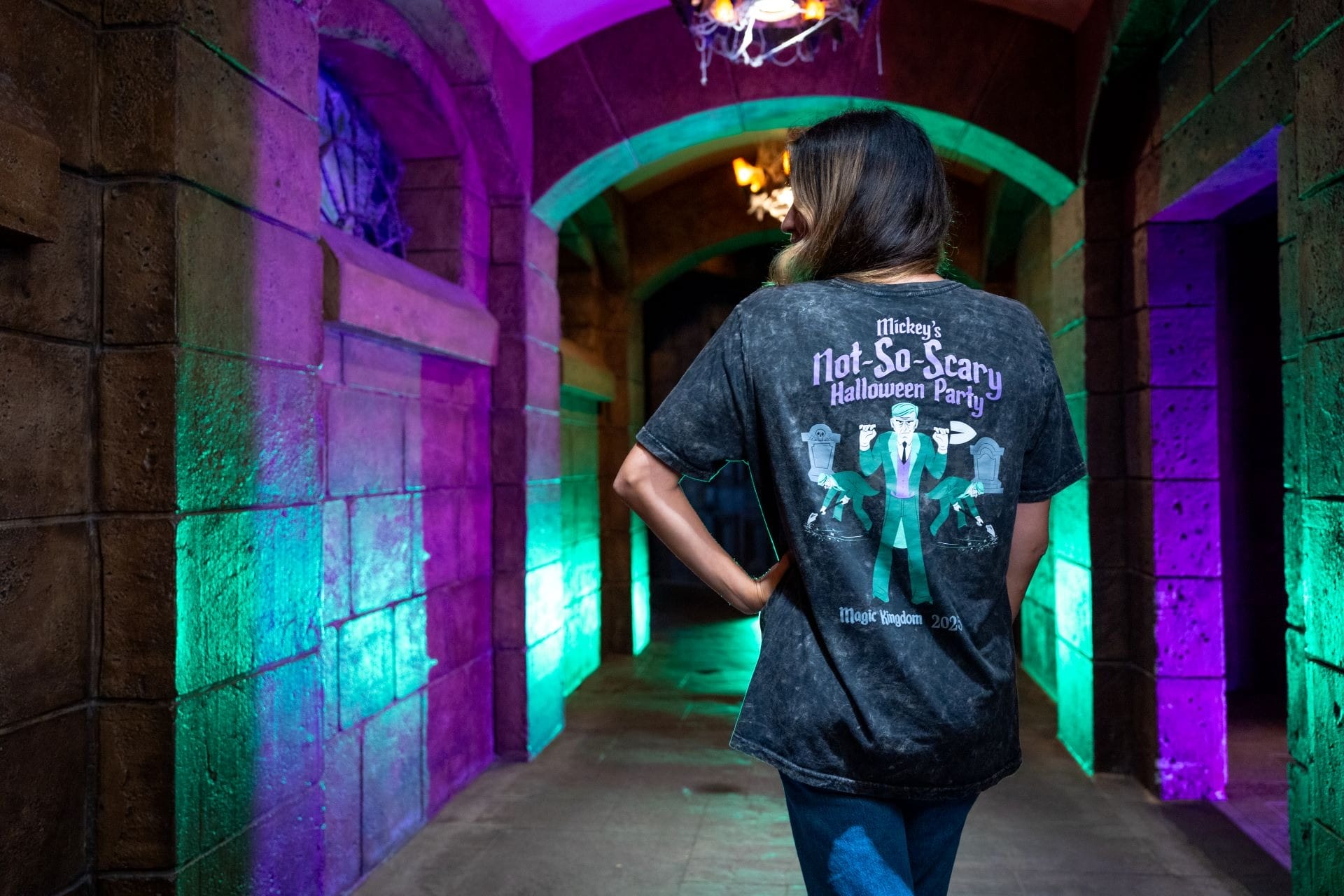 A woman stands in a spooky, colorful hallway wearing exclusive Disney merchandise from Mickey's Not-So-Scary Halloween Party.