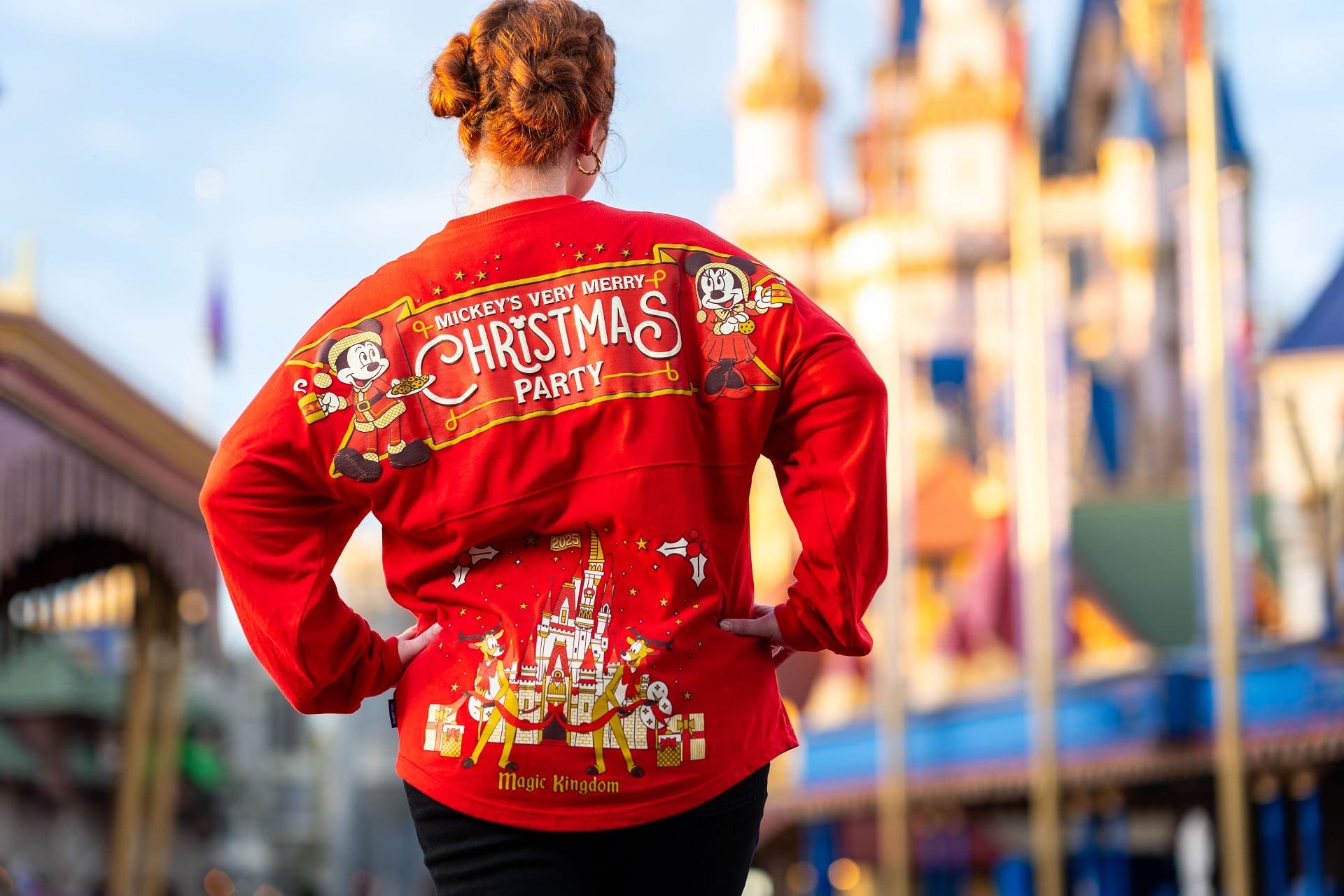 A person in a red "Mickey’s Very Merry Christmas Party" shirt stands in front of a Disney castle.