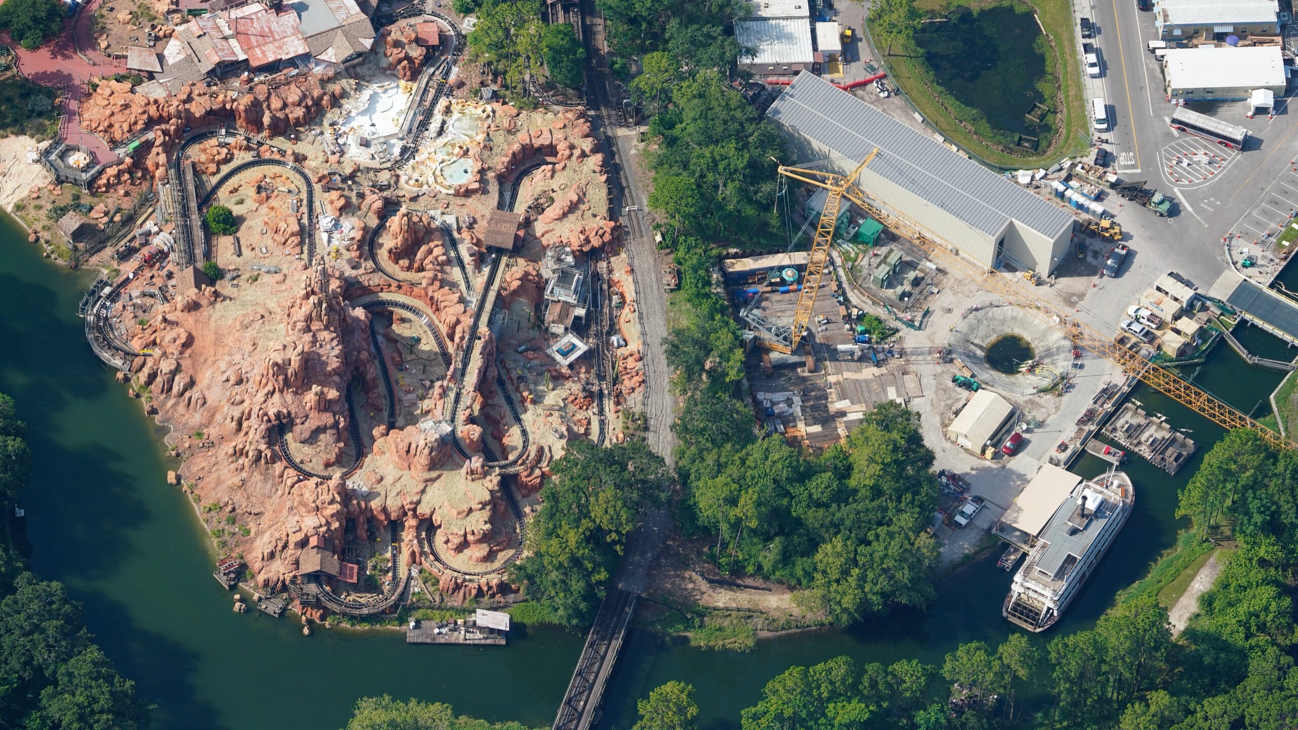 Aerial view of a winding Magic Kingdom ride near Tom Sawyer Island, with trees, water, and nearby construction areas.