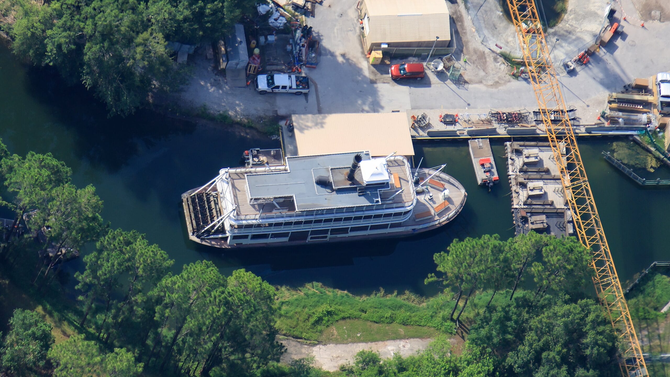 Aerial view of the Liberty Square Riverboat docked near Tom Sawyer Island, surrounded by trees and equipment.