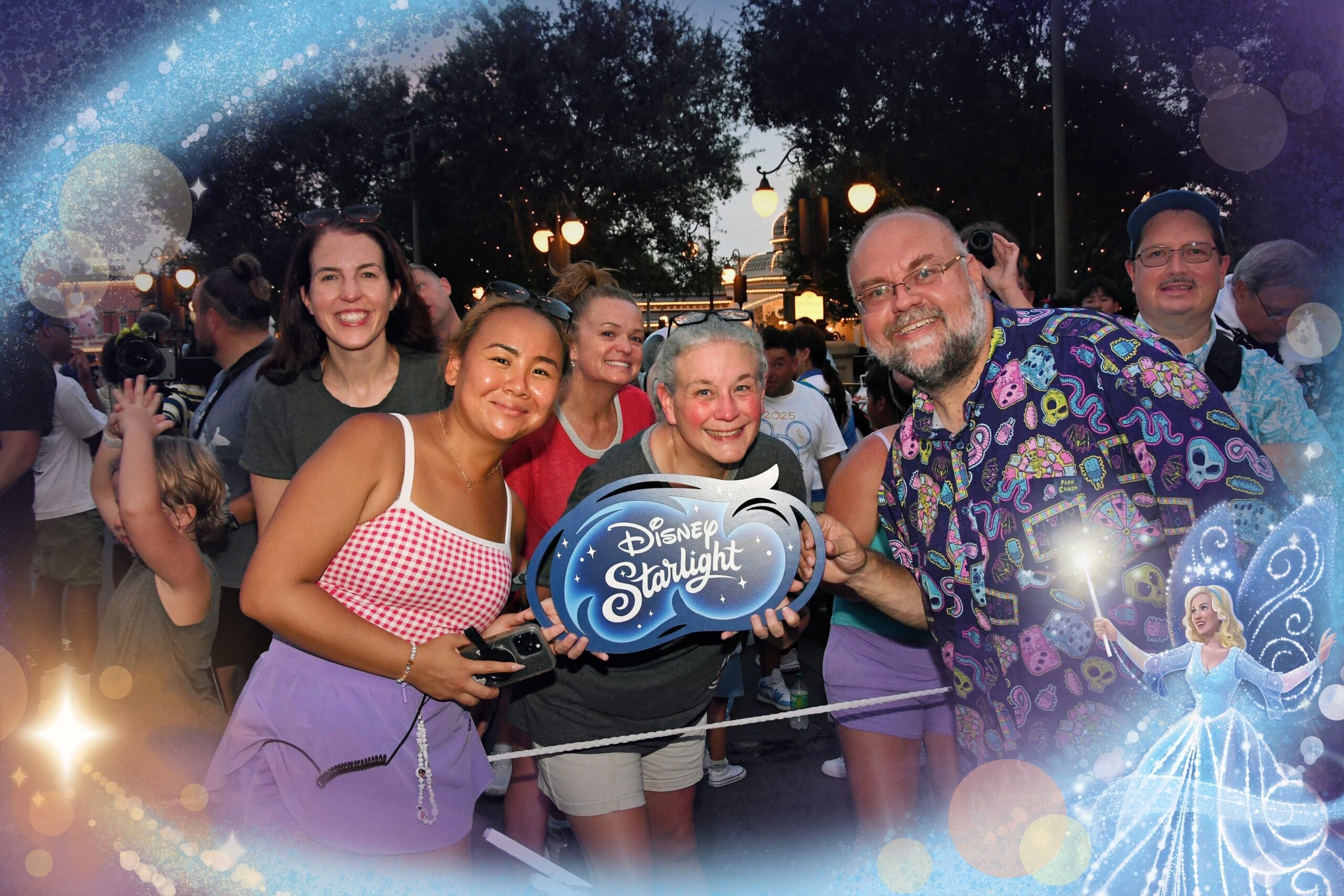 A smiling group holds a “Disney Starlight Parade” sign at an outdoor event, with fairy lights and magical effects.