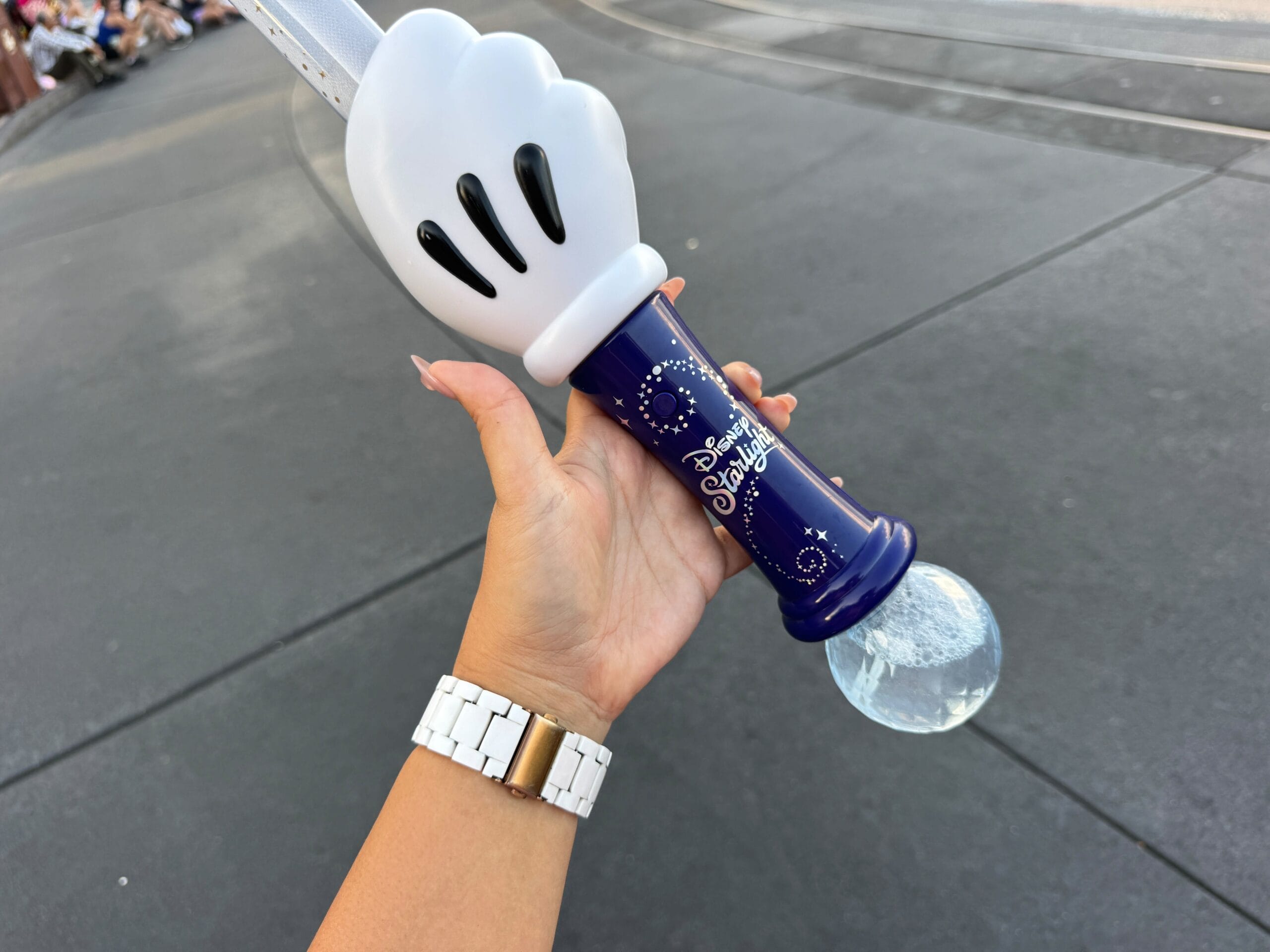 A hand holds a Disney souvenir wand with a Mickey glove handle and "Disney Stars" text on a blue handle.
