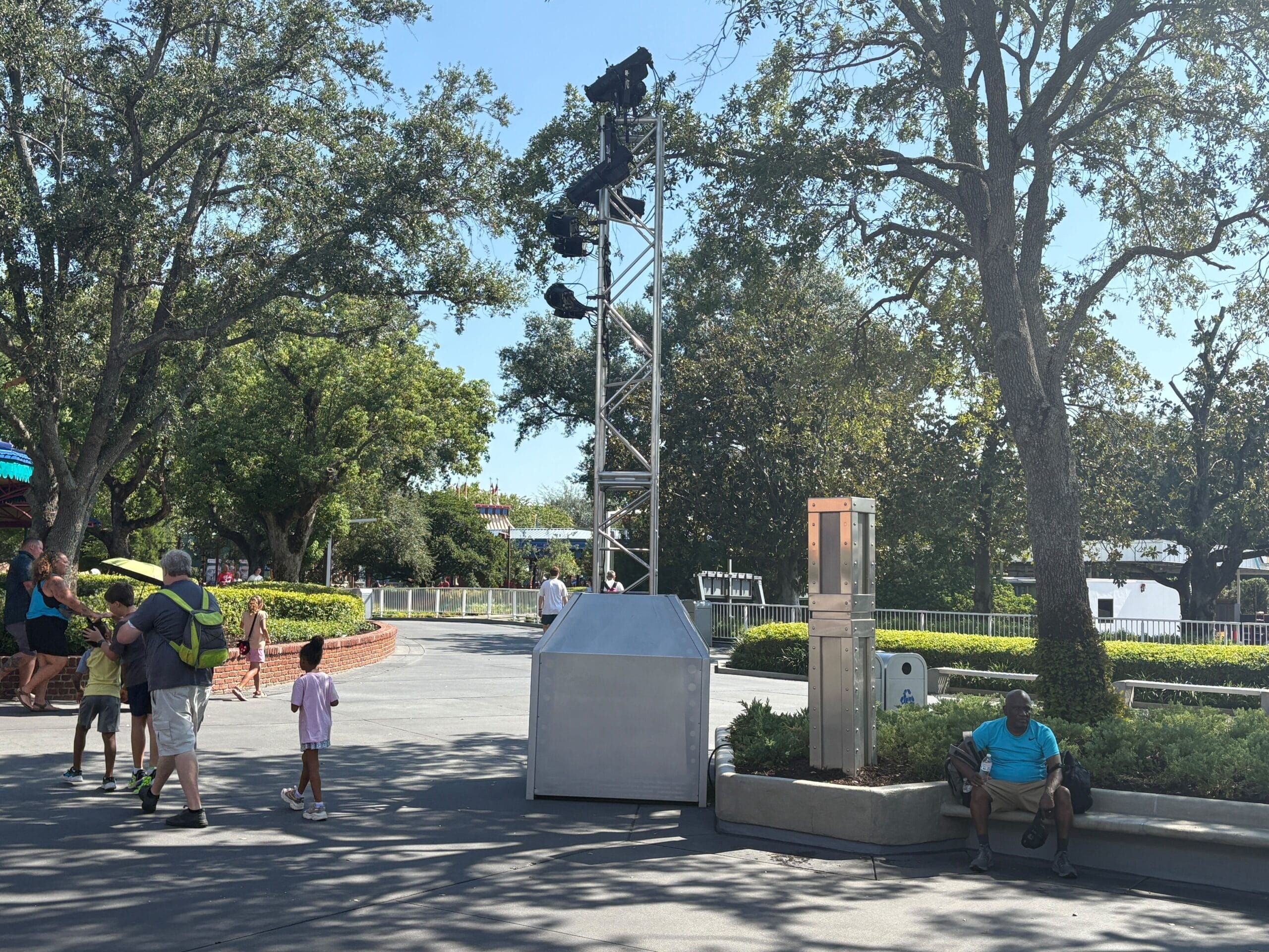 People walk and sit in Magic Kingdom with trees and new trusses on the silver metal structure in the center.