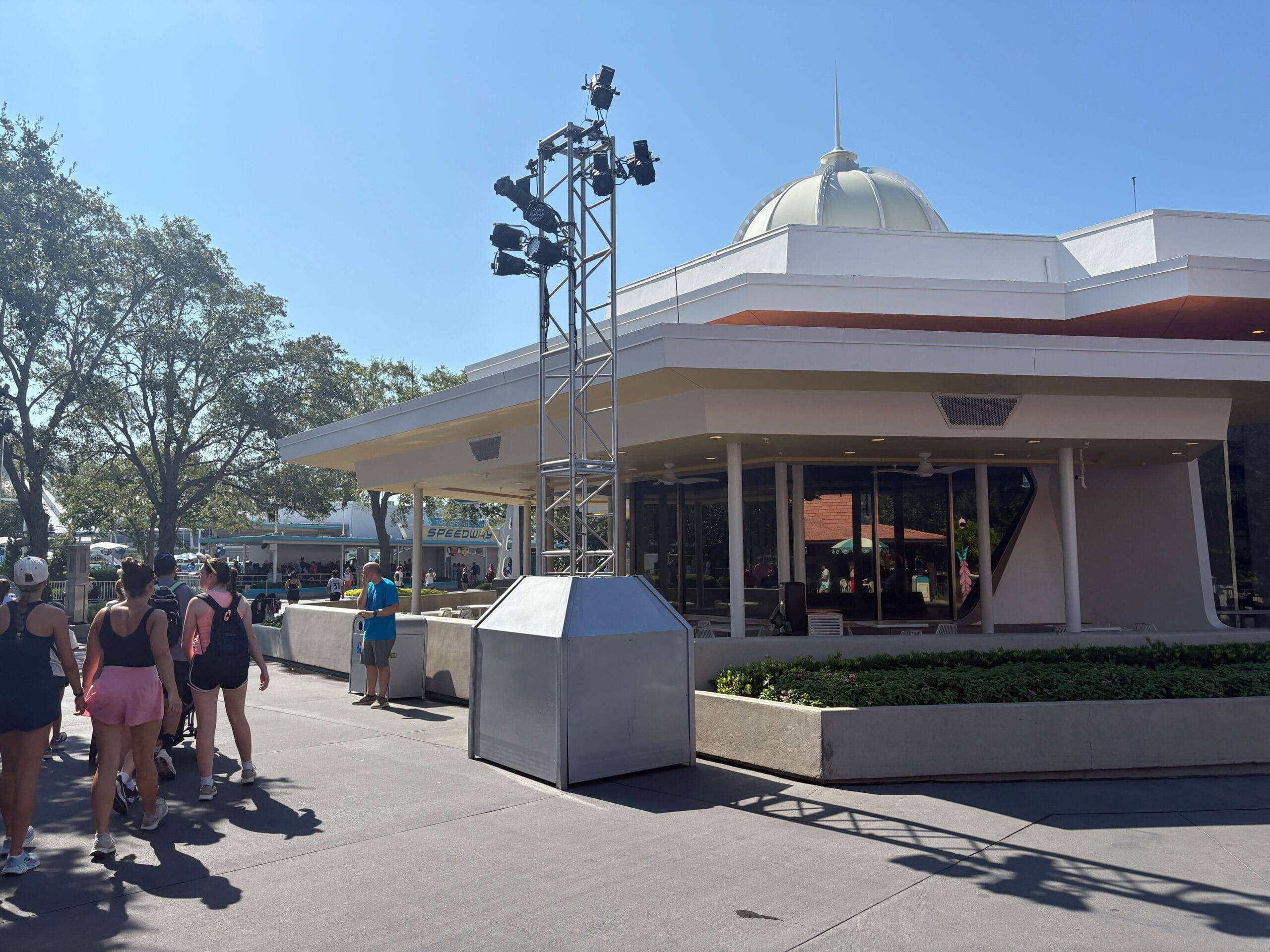A group walks past Cosmic Ray's Starlight Cafe, with trusses and lighting on a sunny day.