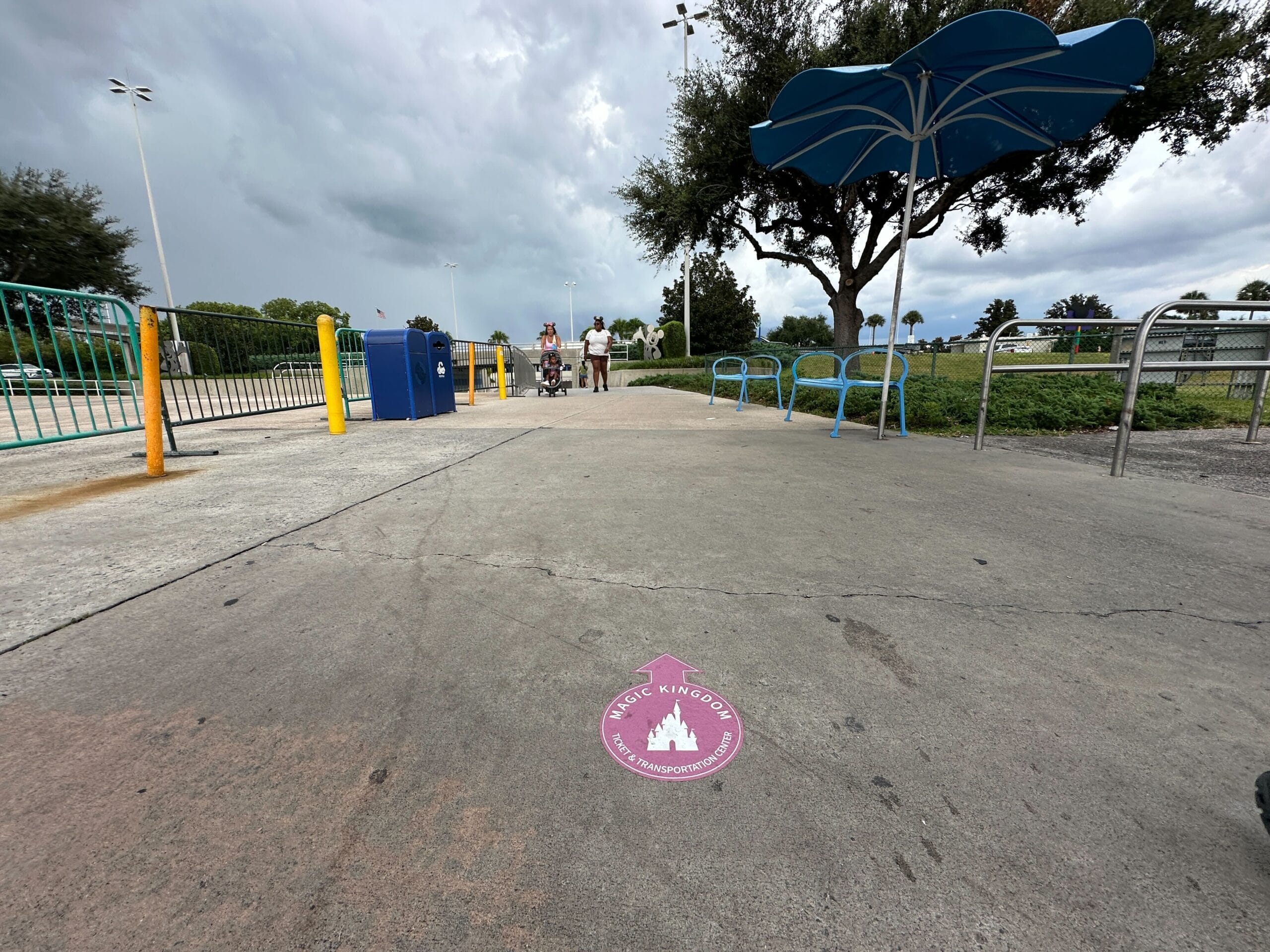 A sidewalk with a "Magic Kingdom" sticker, bike racks, and parking lot decals under a cloudy sky.